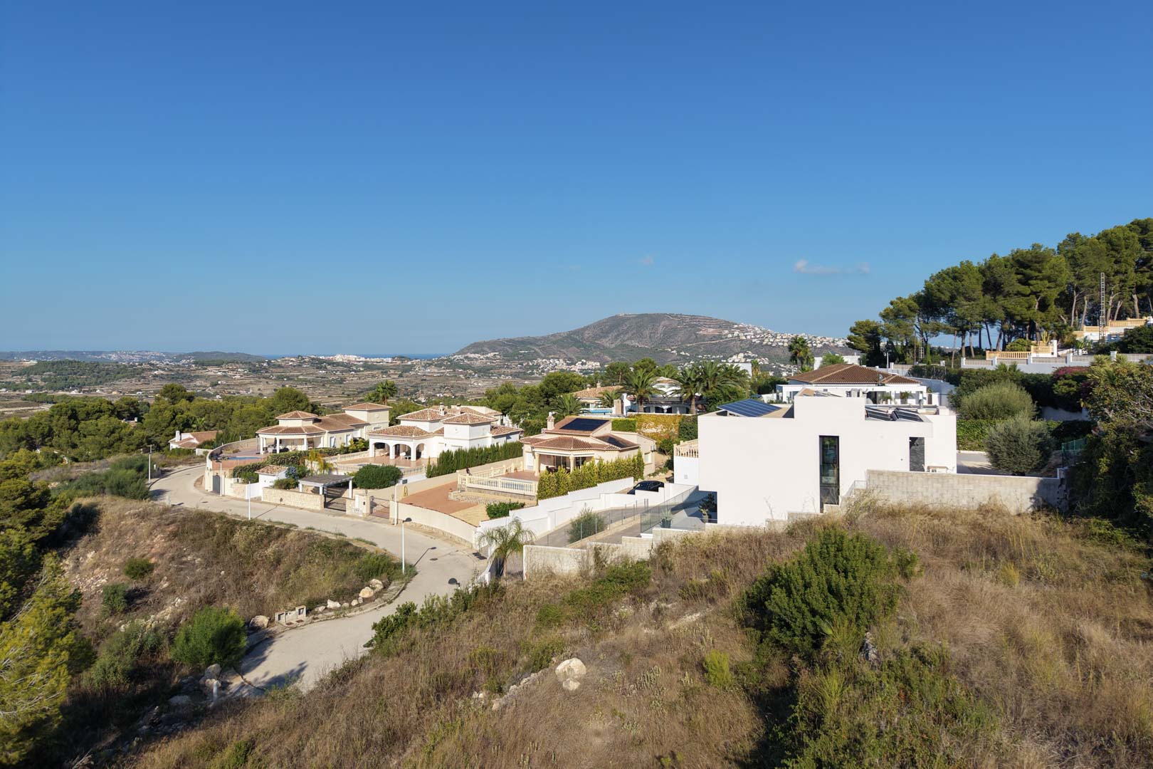 Erhöhter Panoramablick auf das Wohngebiet mit Hanglage und weitem Ausblick auf die umliegenden Berge und das Mittelmeer am Horizont.