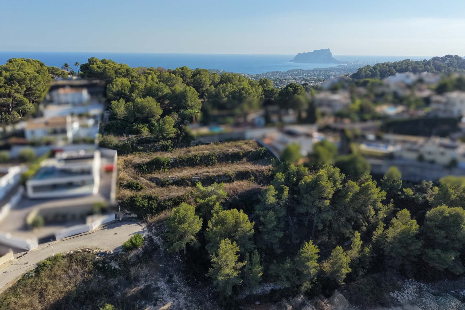Terrassiertes Baugrundstück mit Steinmauern und Pinien, das einen weiten Blick auf das Mittelmeer und den markanten Peñón de Ifach bietet.
