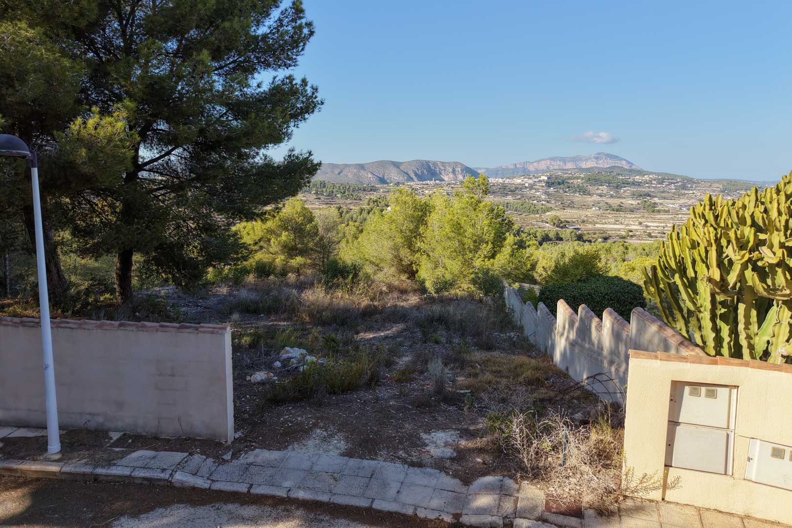 Erhöhtes Stadtgrundstück in Benimeit mit freiem Blick auf das Tal und die Berge. Es verfügt über Begrenzungsmauern, mediterrane Vegetation und Zugang über eine befestigte Straße.