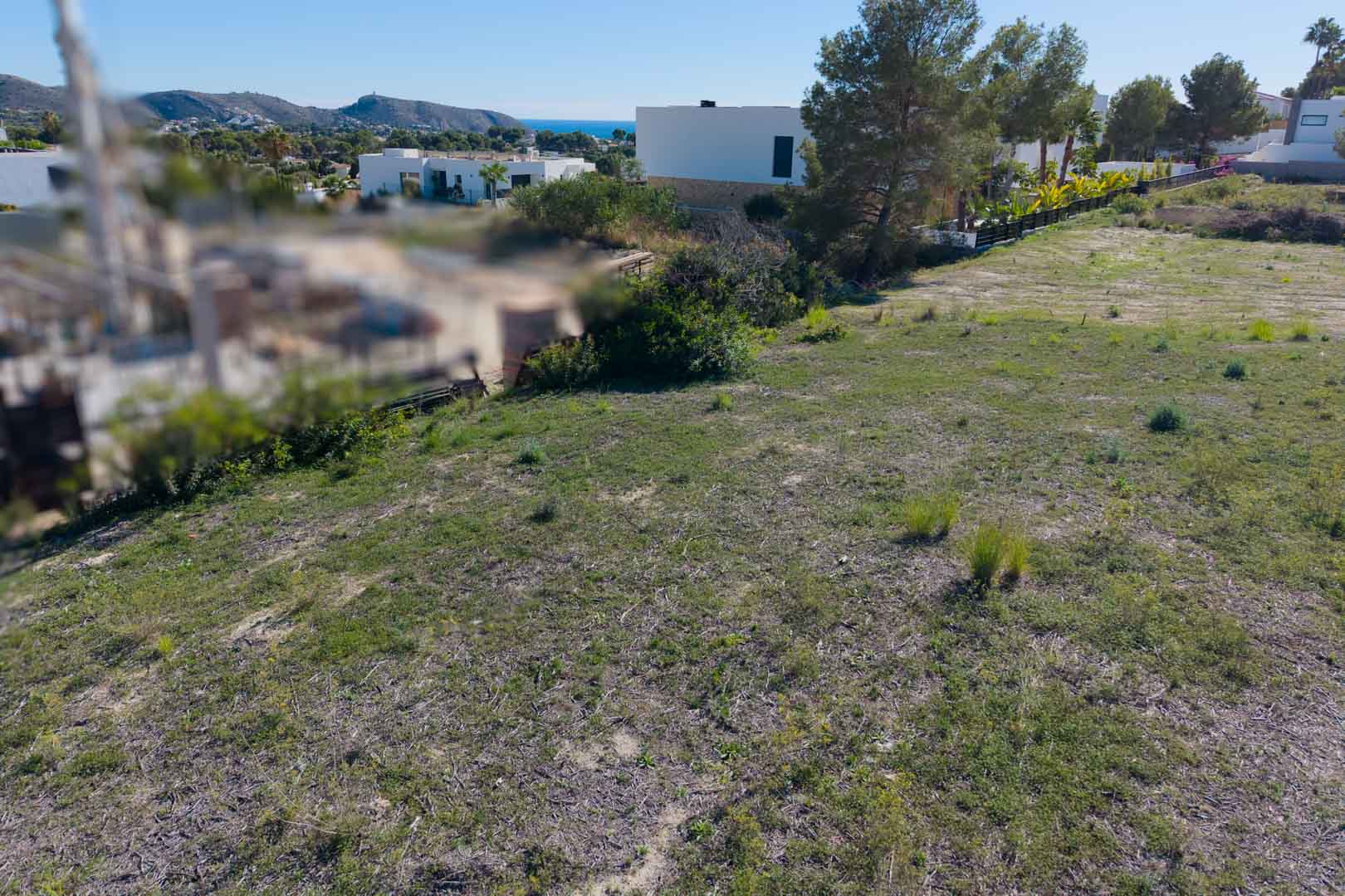 Ebenes Baugrundstück in El Tesoro, Moraira, mit Blick auf das Tal und das Meer, umgeben von moderner Architektur und mediterraner Flora.