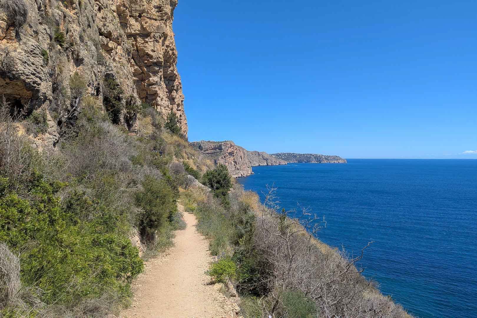 Küstenwanderweg entlang von Kalksteinfelsen mit Panoramablick auf das Mittelmeer und die zerklüftete Küstenlinie von Moraira.