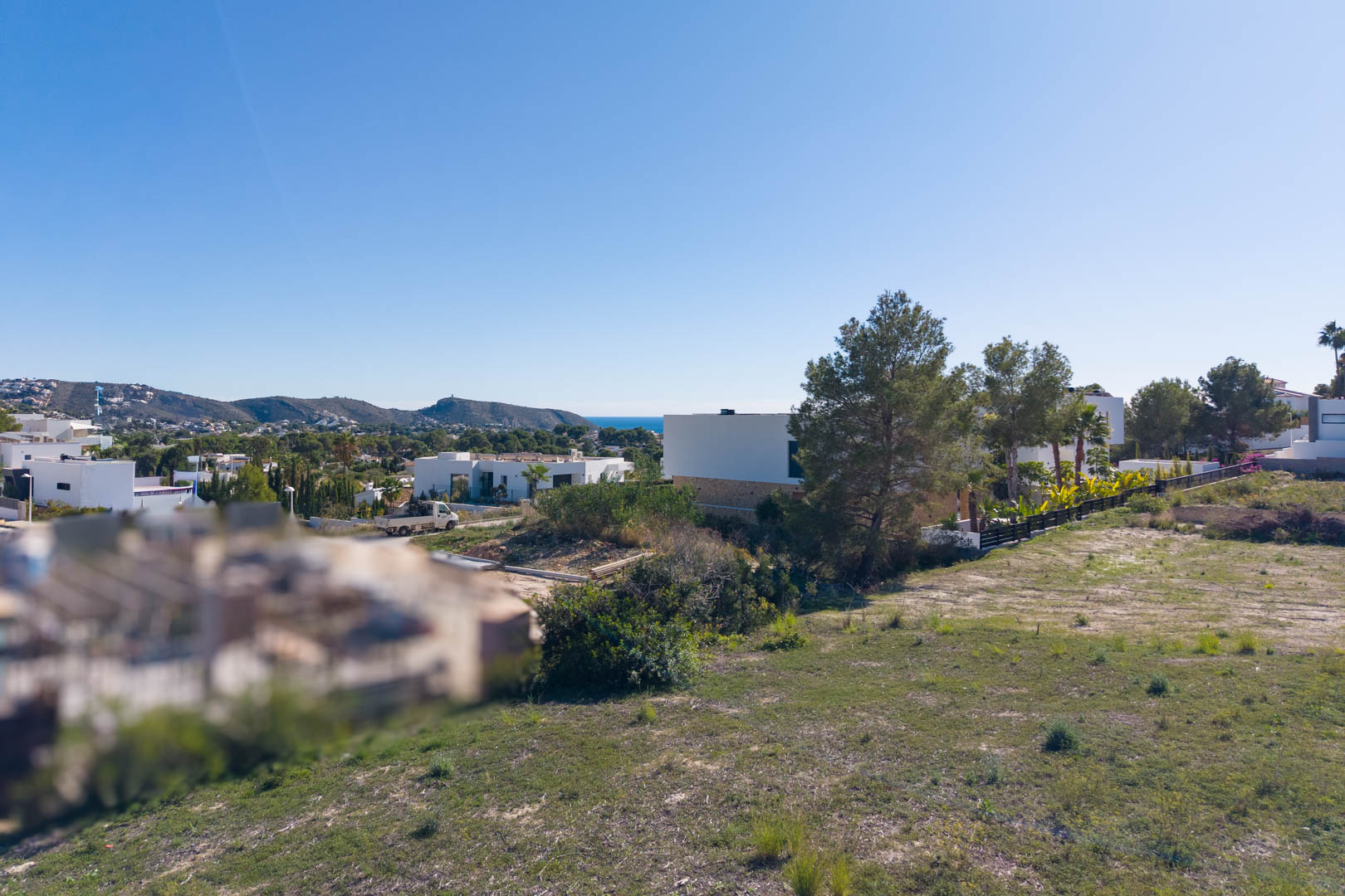 Panoramablick vom Baugrundstück in El Tesoro mit ebenem Gelände, modernen Villen in der Nachbarschaft und weitem Blick über das Tal bis zum Meer.