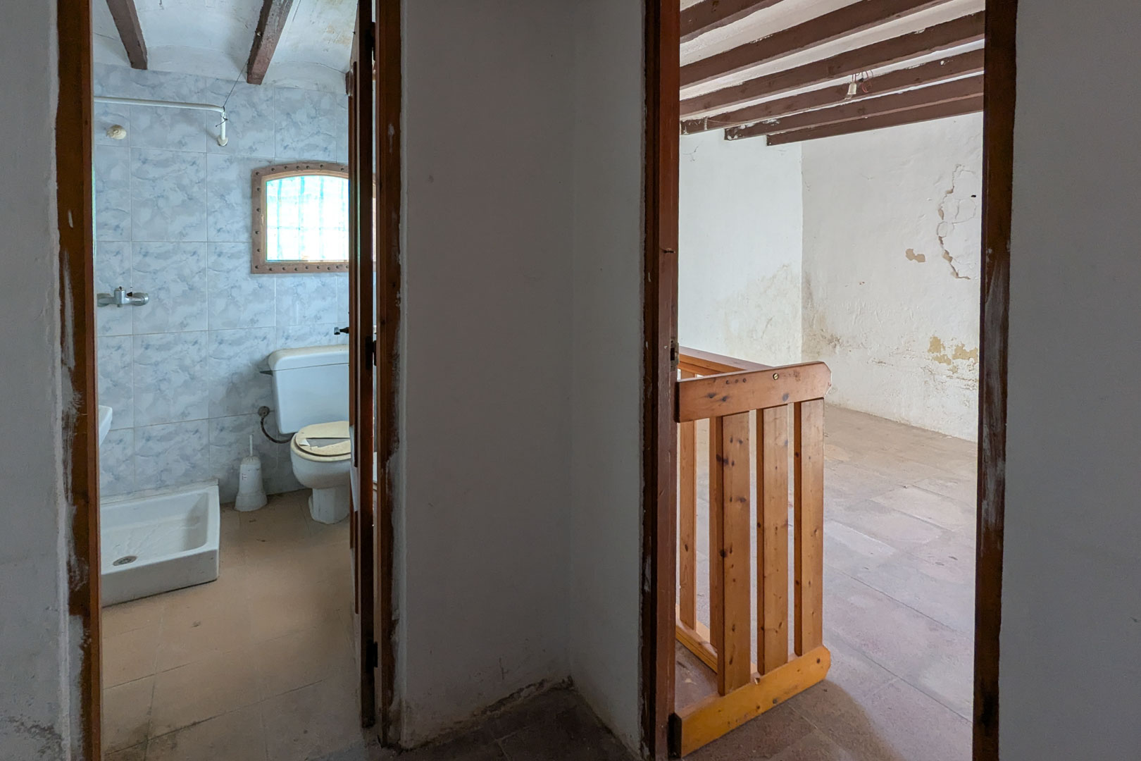 Ansicht des Obergeschosses mit einem gefliesten Badezimmer und einem angrenzenden Raum mit sichtbaren Holzbalken und Kieferngeländer.