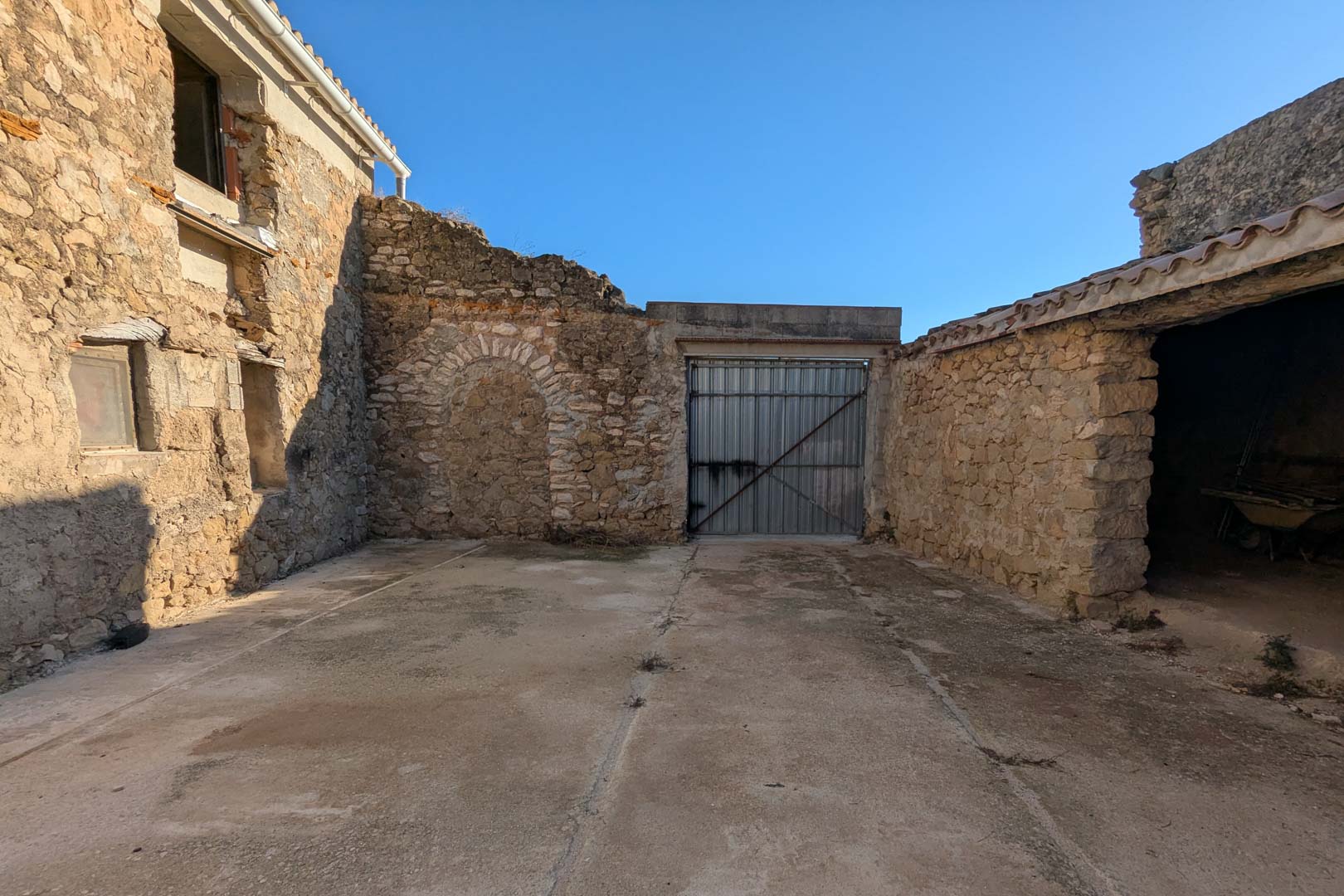 Außenhof mit traditionellem Natursteinmauerwerk, einem zugemauerten Rundbogen und Zugang zu den historischen Stallungen.
