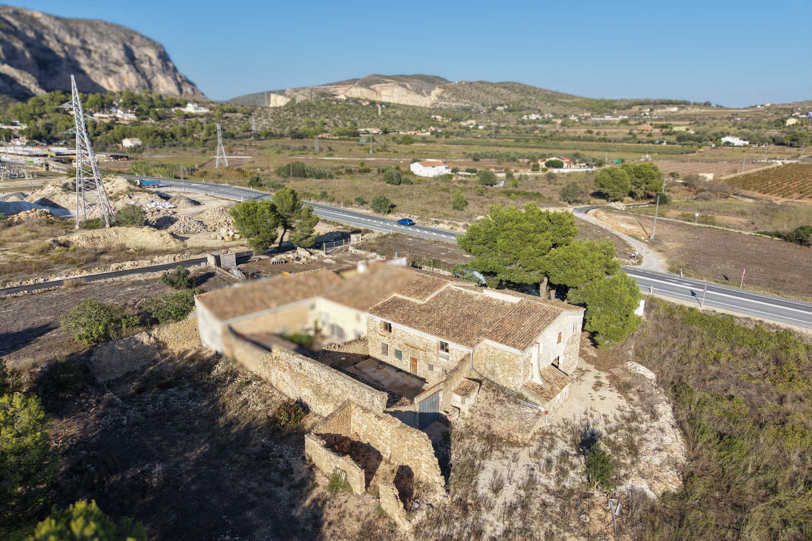 Luftaufnahme des traditionellen Steinbauernhauses mit Terrakottadach, Innenhof und flachem Grundstück vor einer markanten Bergkulisse in Teulada.