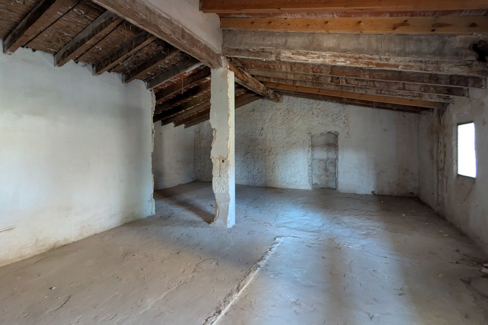 Offenes Obergeschoss mit originalen Mandelholzbalken, Schilfrohrdecken und kalkverputzten Steinwänden sowie einem seitlichen Fenster.