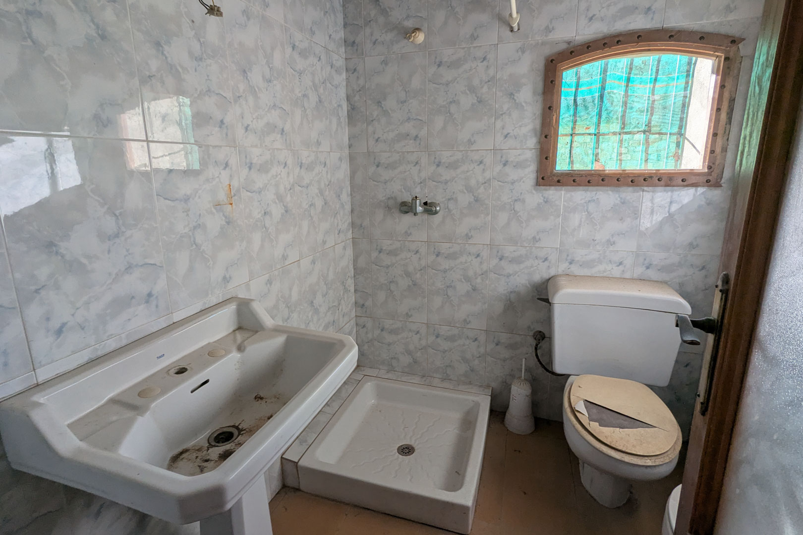 Originales Badezimmer mit blau marmorierten Wandfliesen, Standwaschbecken, quadratischer Duschwanne und einem kleinen Rundbogenfenster mit Holzrahmen.
