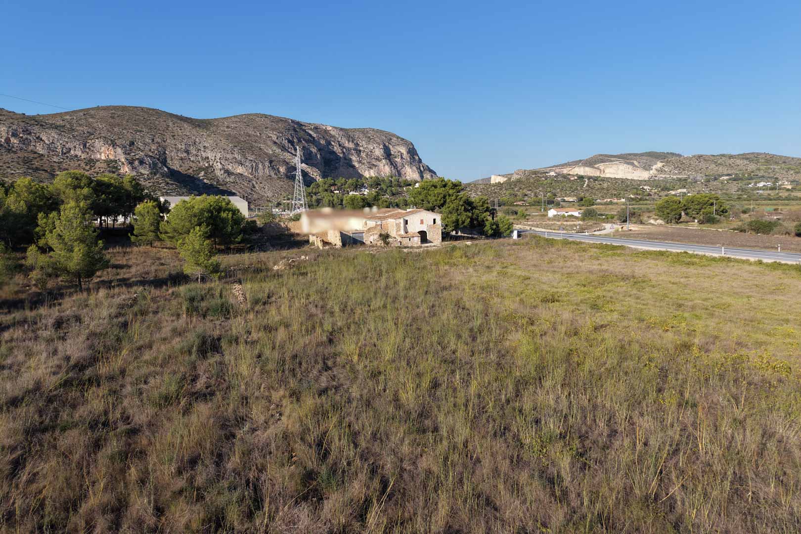 Panoramablick auf das traditionelle Steinhaus auf einem weitläufigen ländlichen Grundstück, umgeben von mediterraner Vegetation und Bergen in Teulada.