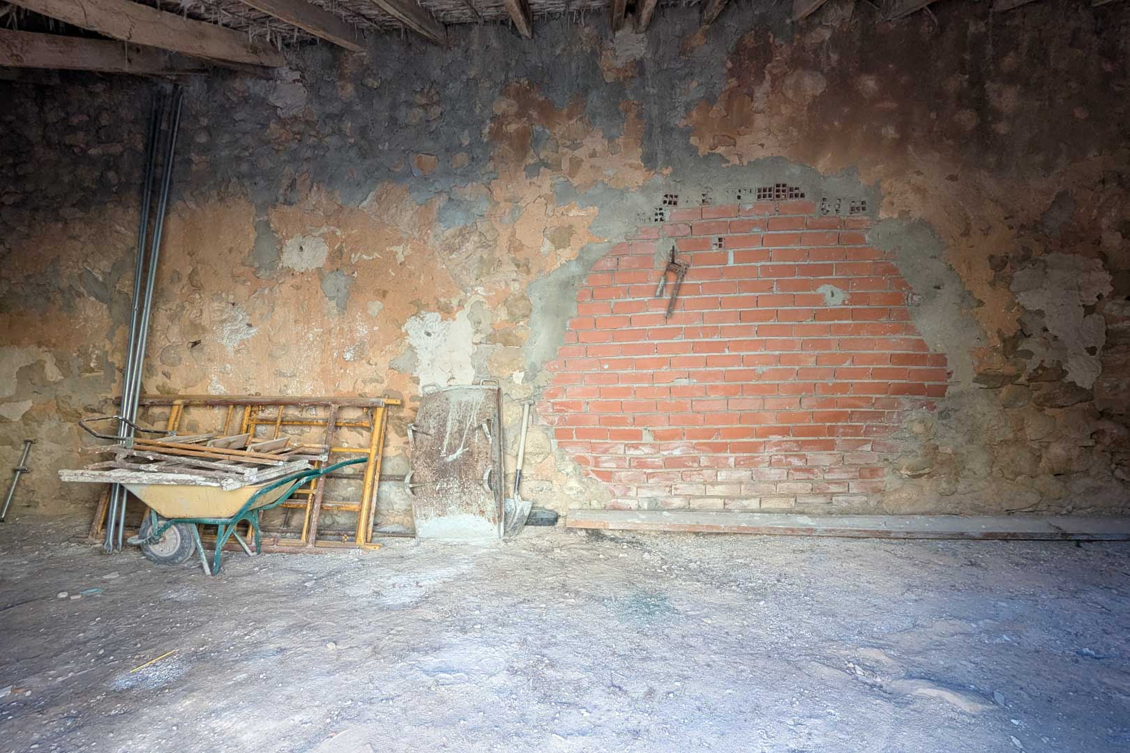 Rustikaler Innenraum mit originalen Steinwänden, einem Ziegelabschnitt und einer traditionellen Decke aus Holzbalken und Schilfrohr. Der Raum dient derzeit als Lager.
