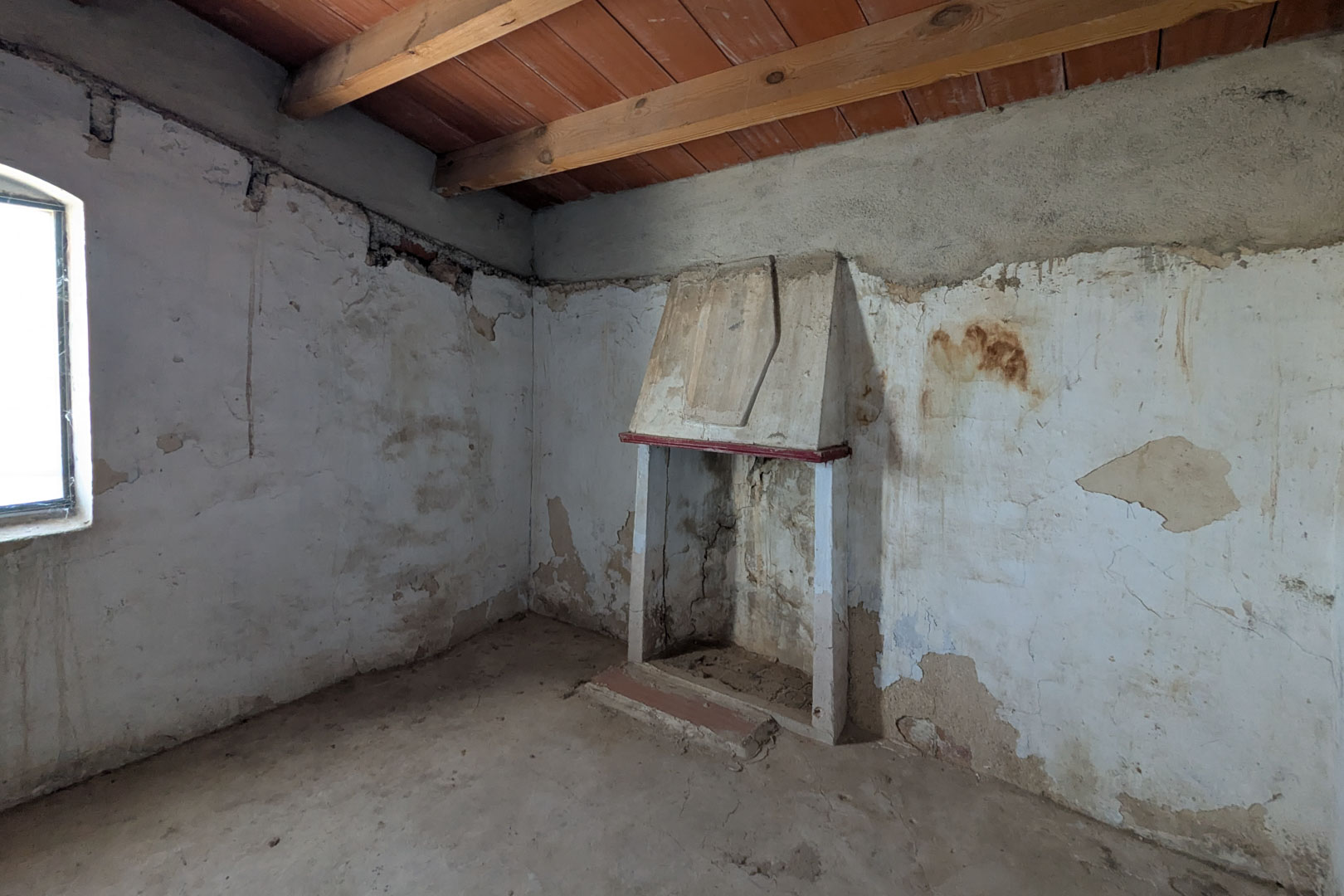 Rustikaler Wohnbereich mit traditionellem Kamin, sichtbaren Holzdeckenbalken und kalkverputzten Wänden, die den ursprünglichen Charakter bewahren.