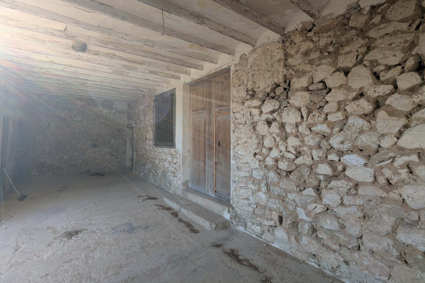 Überdachte Veranda mit freigelegten Natursteinwänden, originalen Holzbalkendecken und einer traditionellen hölzernen Doppeltür im rustikalen Stil.