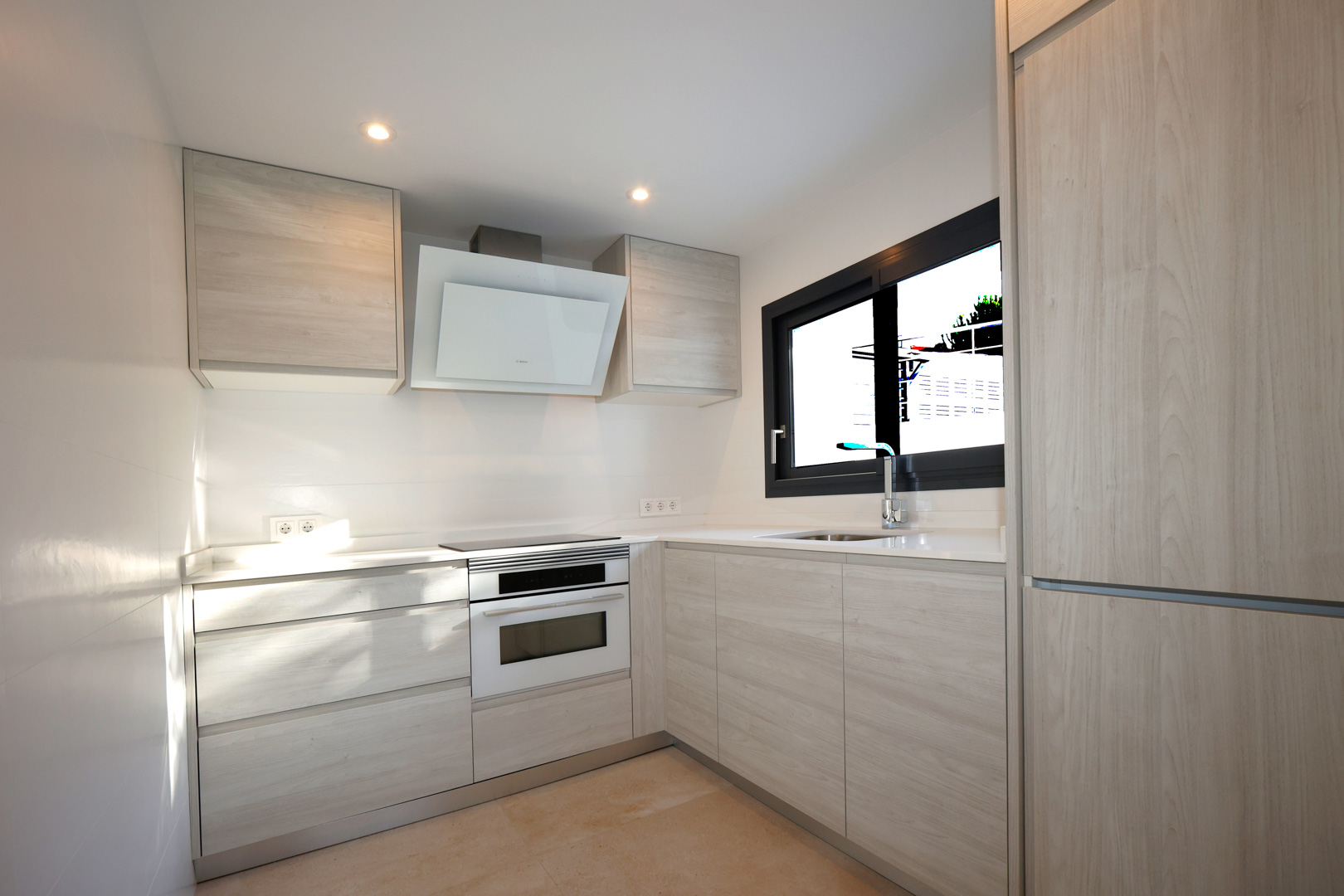 Funktionale Küche mit hellen Holzmöbeln, weißer Silestone-Arbeitsplatte, Induktionskochfeld, Bosch-Backofen und dekorativer Dunstabzugshaube.
