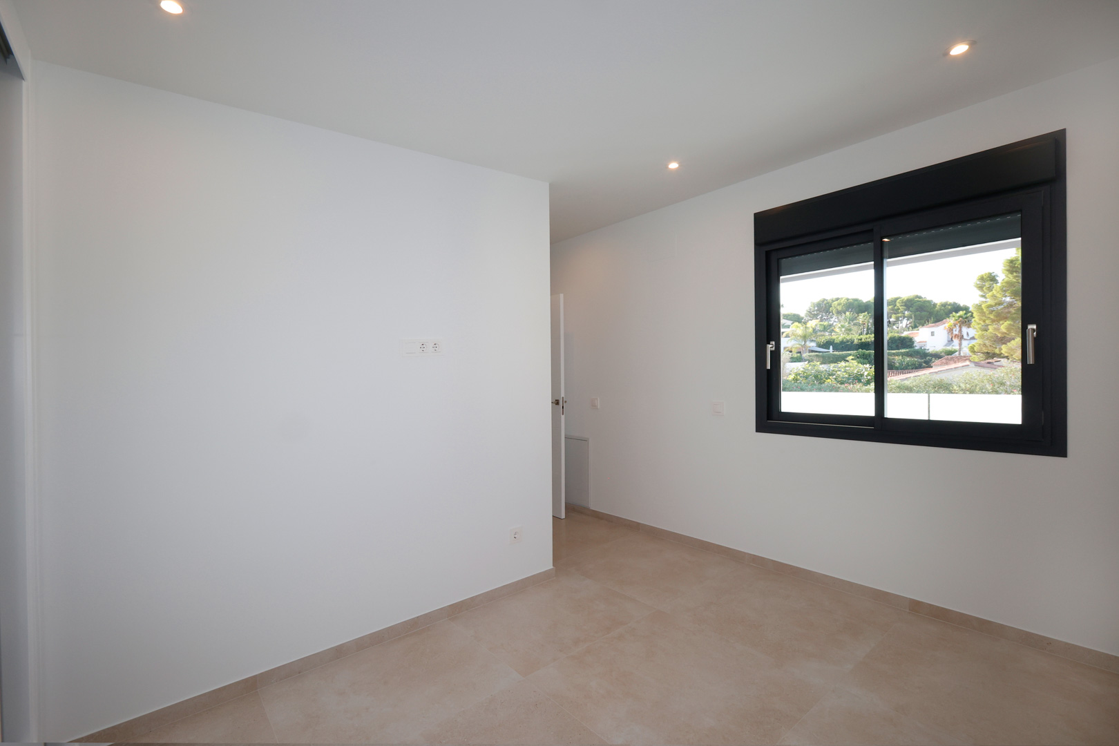 Minimalistisches Schlafzimmer mit weißen Wänden, Feinsteinzeugboden und schwarzem Aluminiumfenster mit elektrischen Jalousien und Blick ins Grüne.