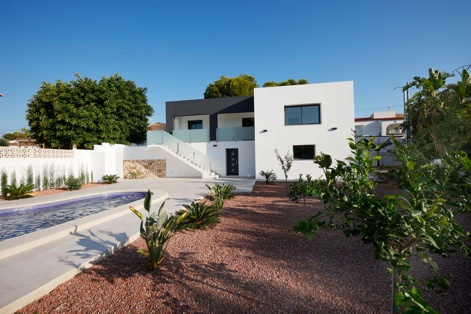 Moderne Fassade mit Pool, rotem Marmorkiesgarten und Außentreppe mit Edelstahl- und Glasgeländer. Mit Natursteinmauern und Technal-Aluminiumfenstern.