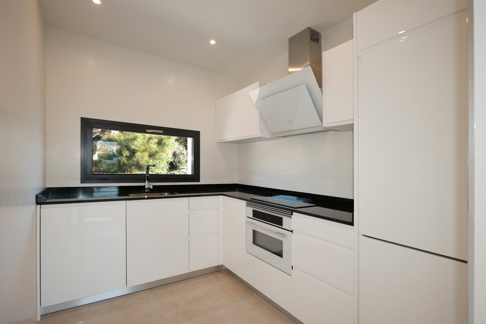 Moderne Küche mit weiß lackierten Schränken, schwarzer Silestone-Arbeitsplatte, integrierten Bosch-Geräten und Fenster mit Gartenblick.