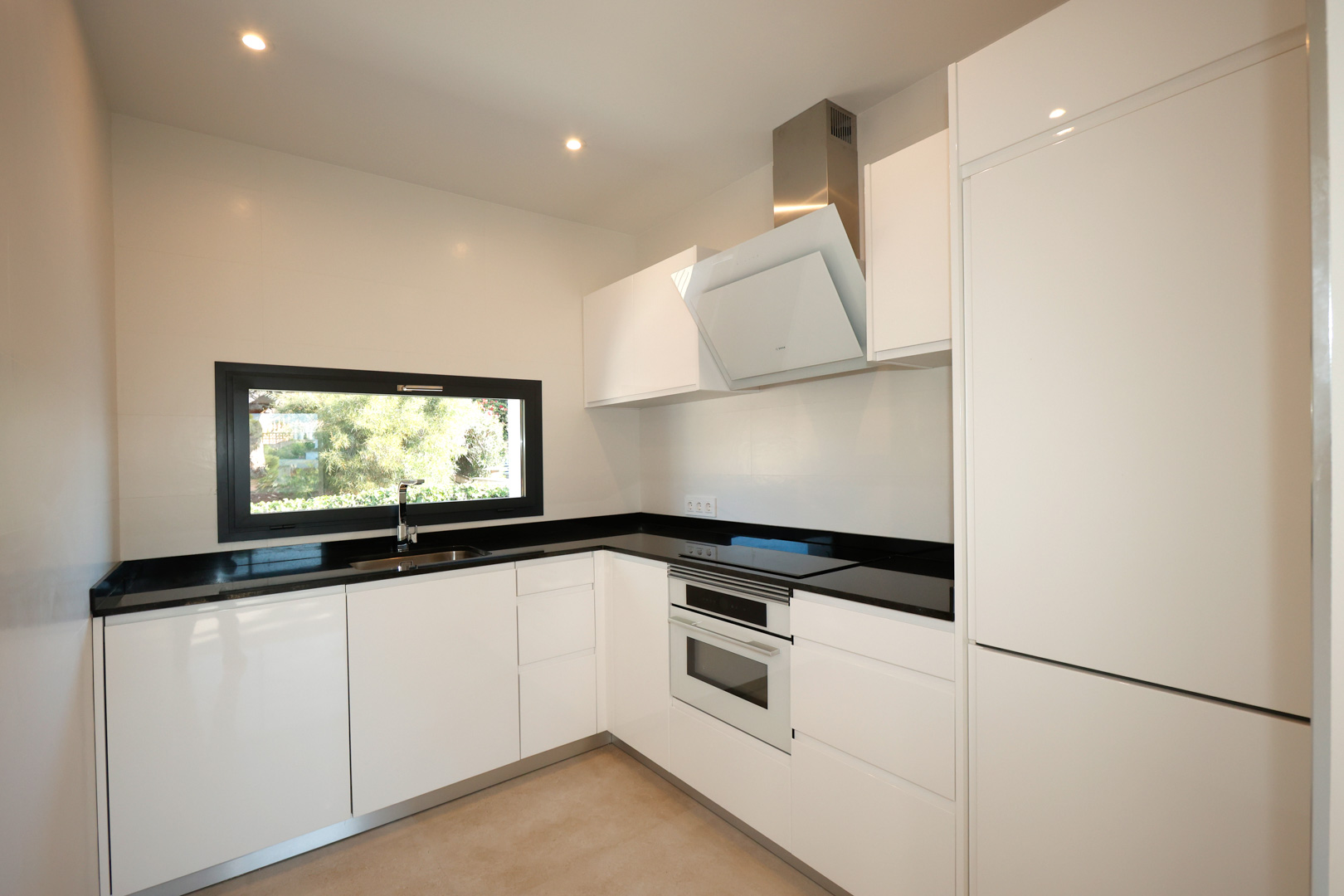 Moderne Küche mit weißen Hochglanzfronten, schwarzer Silestone-Arbeitsplatte, Bosch-Einbaugeräten und Fenster mit Blick ins Grüne.