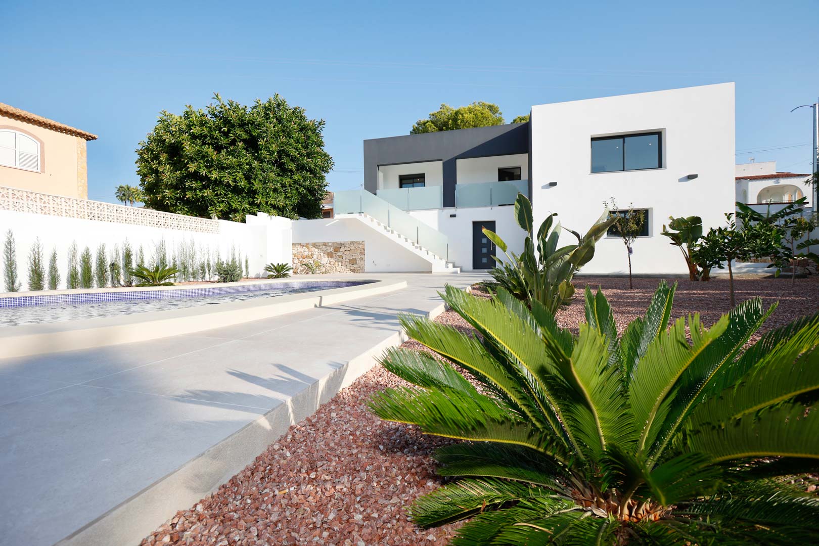 Moderne zweistöckige Villa mit Pool, rotem Marmorkiesgarten und Außentreppe mit Glasgeländer, die zu den separaten Wohneinheiten führt.