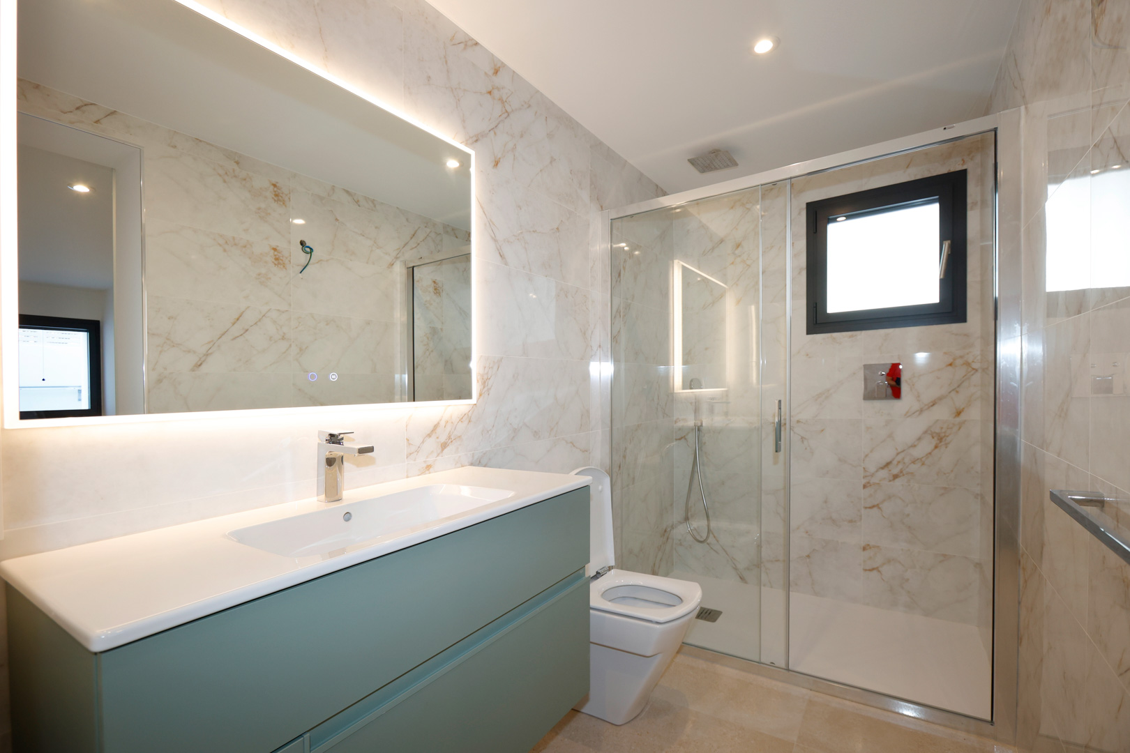 Modernes Badezimmer mit salbeigrünem Waschtisch, LED-hinterleuchtetem Spiegel und begehbarer Glasdusche mit Fliesen in Marmoroptik.