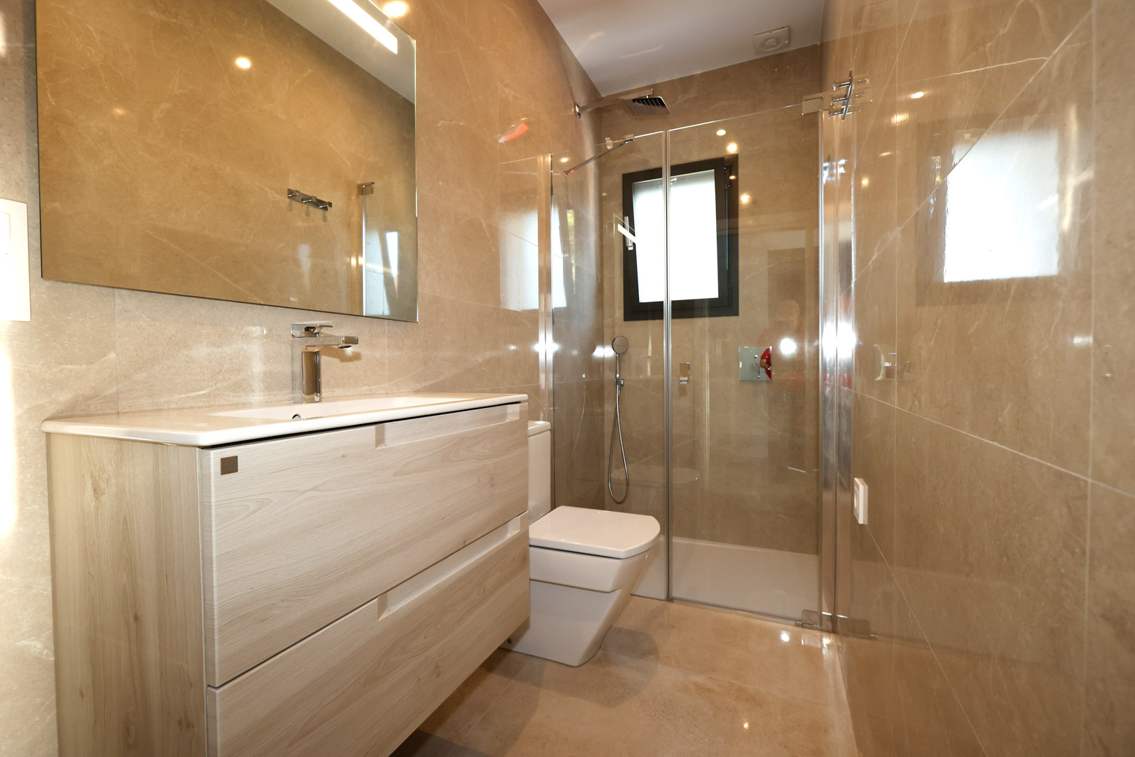 Modernes Badezimmer mit Waschtisch in Holzoptik, Feinsteinzeugwänden in Marmoroptik und einer Glasduschkabine mit verchromten Armaturen.