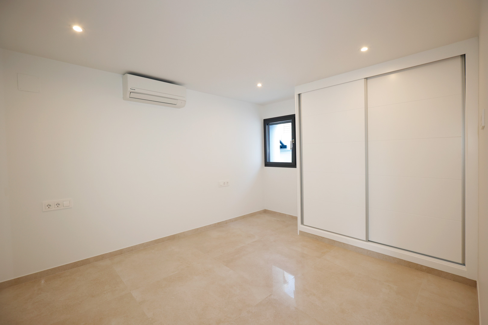 Schlafzimmer mit weißem Schiebetürenschrank, Feinsteinzeugboden, Split-Klimaanlage und in die Decke integrierten LED-Spots.
