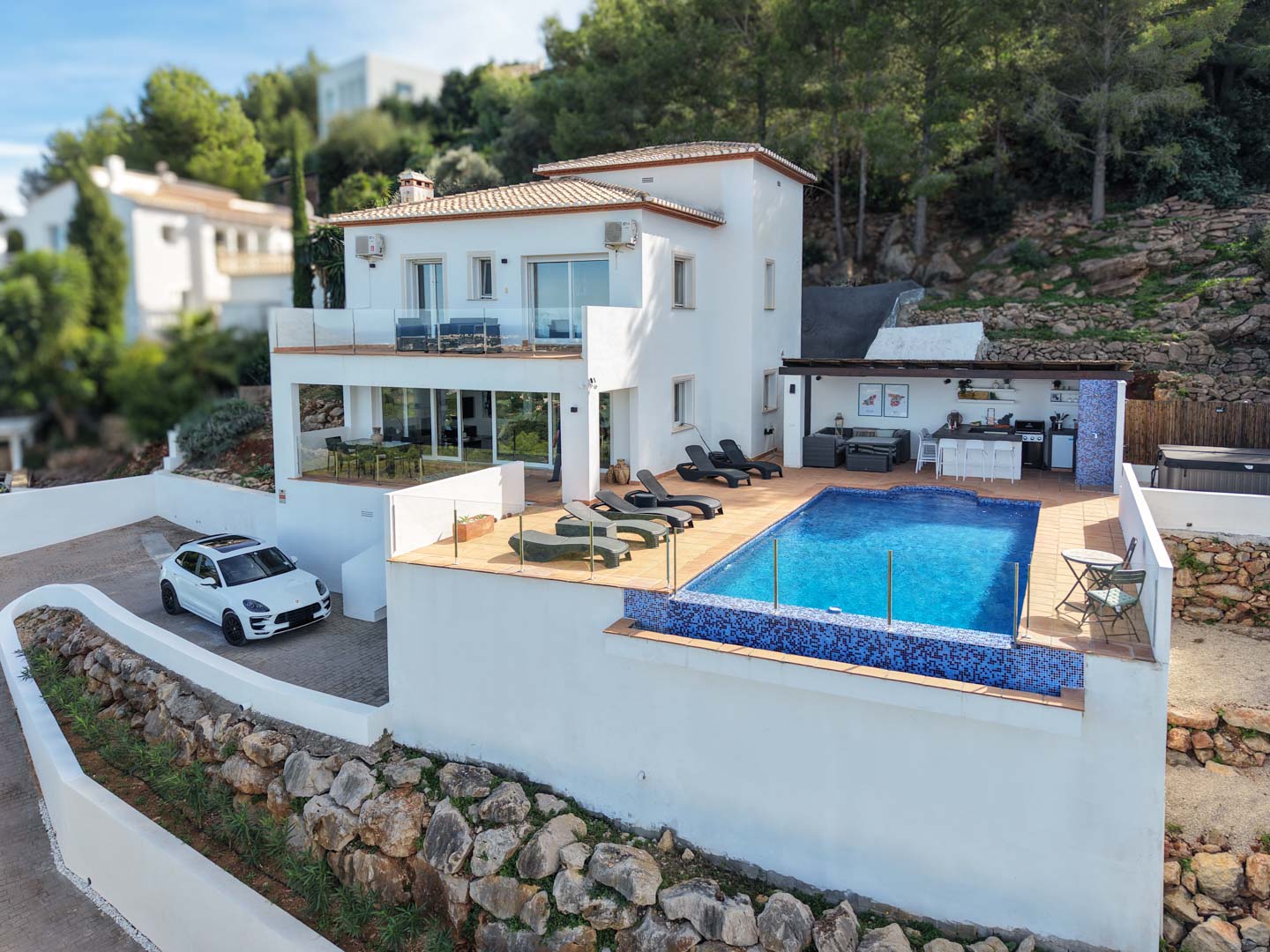 Außenansicht der Villa mit blauem Mosaikpool, großzügiger Sonnenterrasse und ausgestatteter Außenküche, eingebettet in die natürliche Umgebung von La Sella.