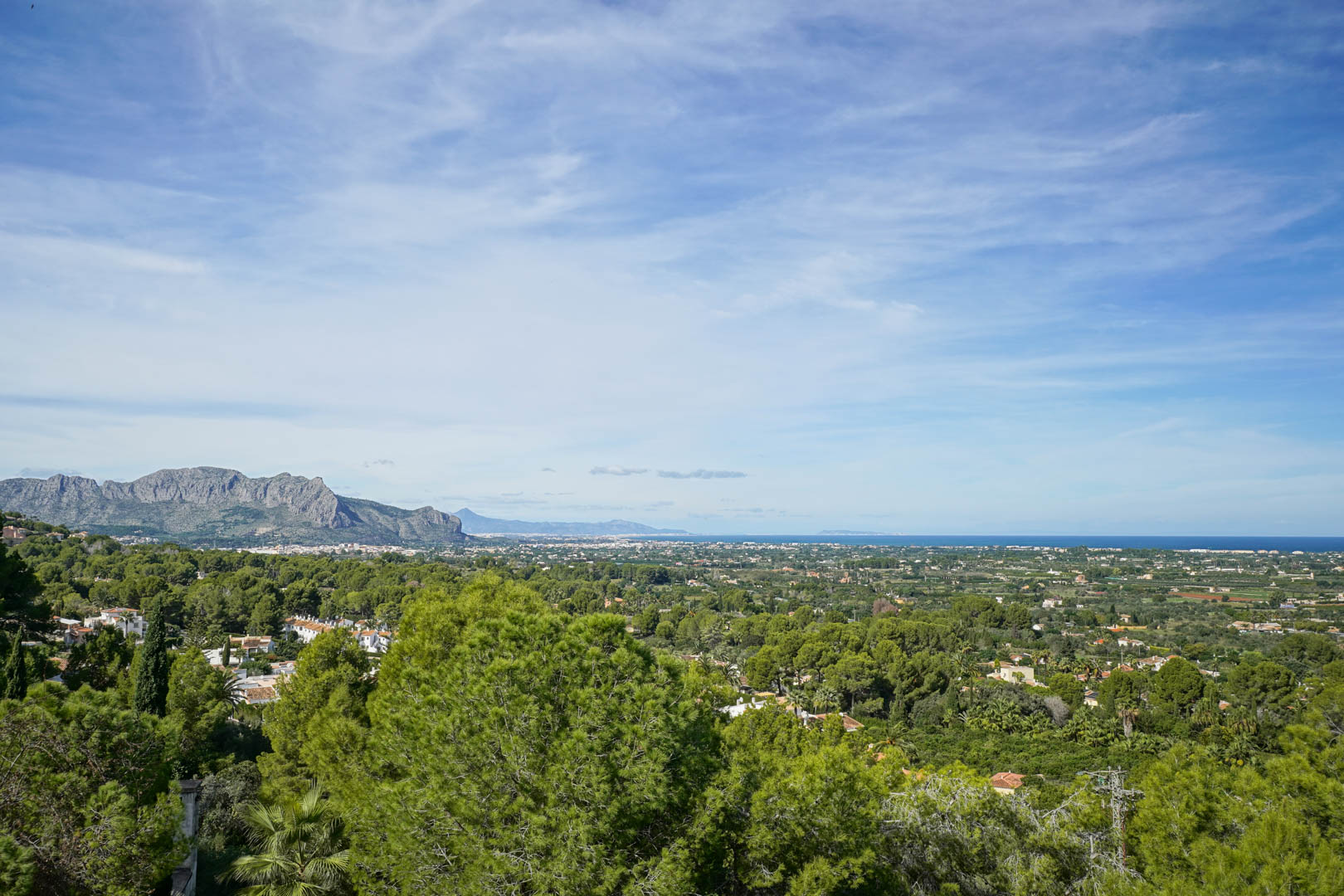 Erhöhter Panoramablick von La Sella auf das Montgó-Massiv, das grüne Küstental und das Mittelmeer am Horizont unter klarem Himmel.