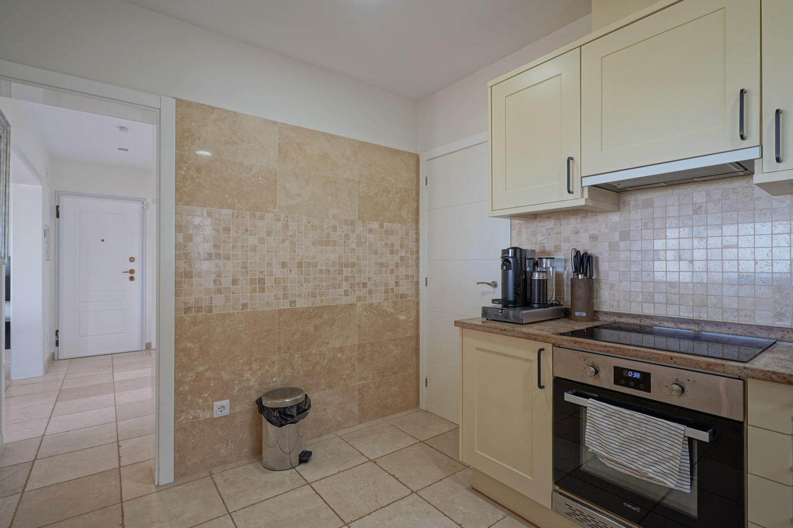 Funktionale Küche mit cremefarbenen Schränken, Granitarbeitsplatte und Einbaugeräten. Die Wand ist mit Naturstein und einem eleganten Mosaikstreifen verkleidet.