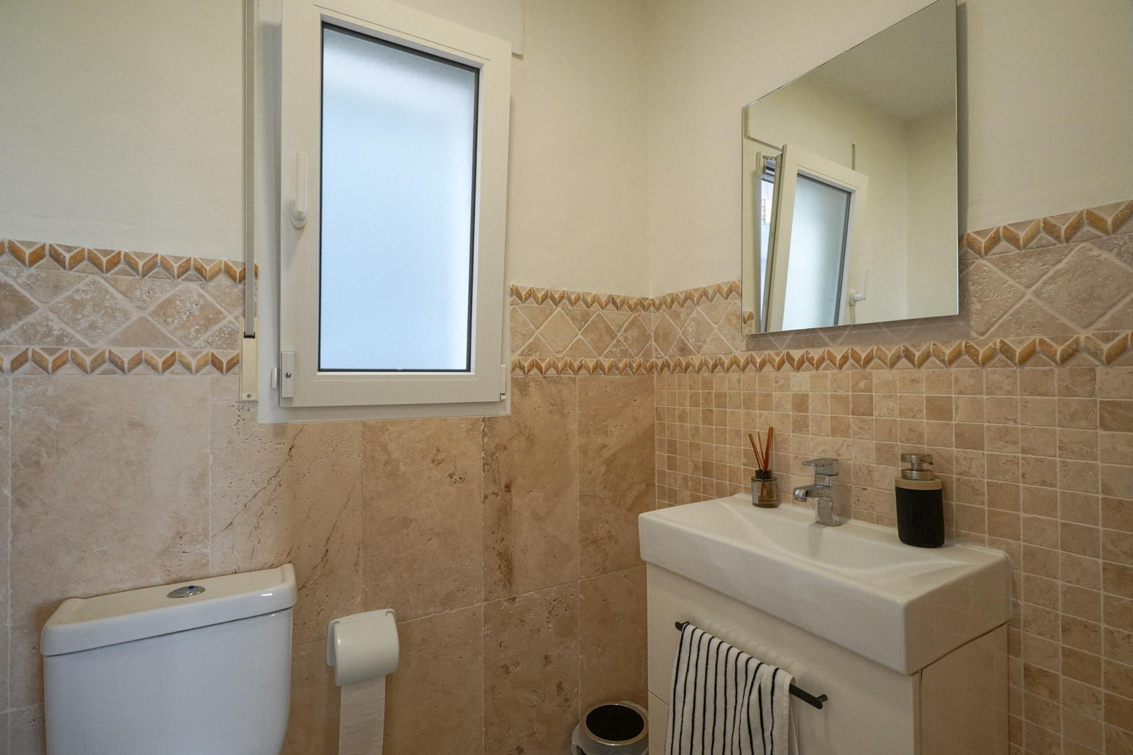Gäste-WC mit erdfarbenen Fliesen, dekorativer Bordüre, modernem Waschbecken und einem Milchglasfenster für natürliches Licht.