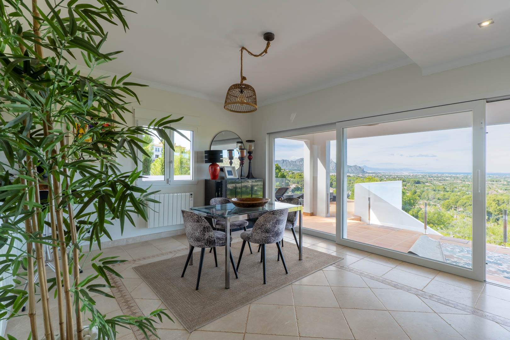 Heller Essbereich mit Glastisch und großen Schiebetüren, die auf eine Terrasse mit Panoramablick auf das Meer und die Berge führen.