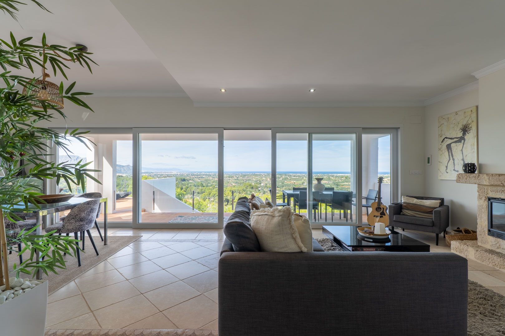 Heller Wohn-Essbereich mit großen Glasschiebetüren, Panoramablick auf das Meer, einem Natursteinkamin und direktem Zugang zur Terrasse.