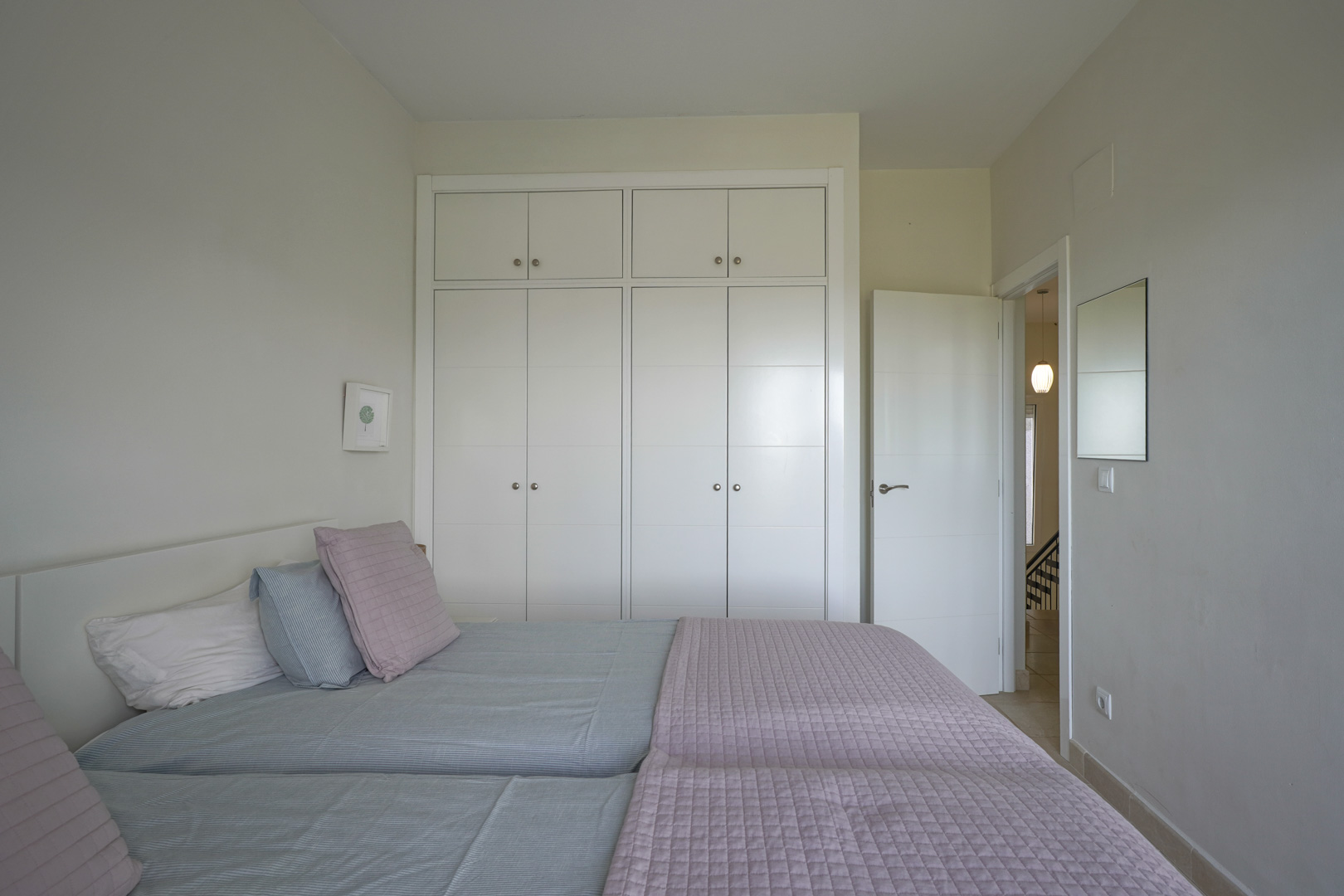 Helles Schlafzimmer mit deckenhohen weißen Einbauschränken und Fliesenboden. Das minimalistische Design besticht durch neutrale Töne und Funktionalität.