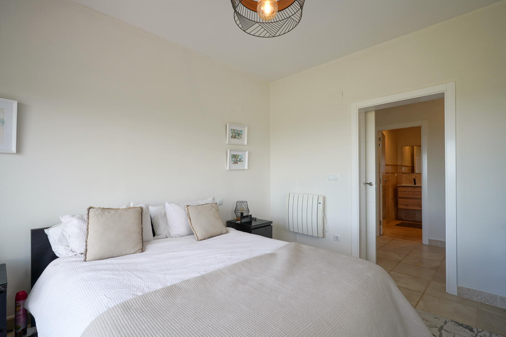 Helles Schlafzimmer mit Keramikfliesen, Doppelbett und direktem Zugang zum En-Suite-Badezimmer. Ausgestattet mit Elektroheizkörper und moderner Pendelleuchte aus Draht.
