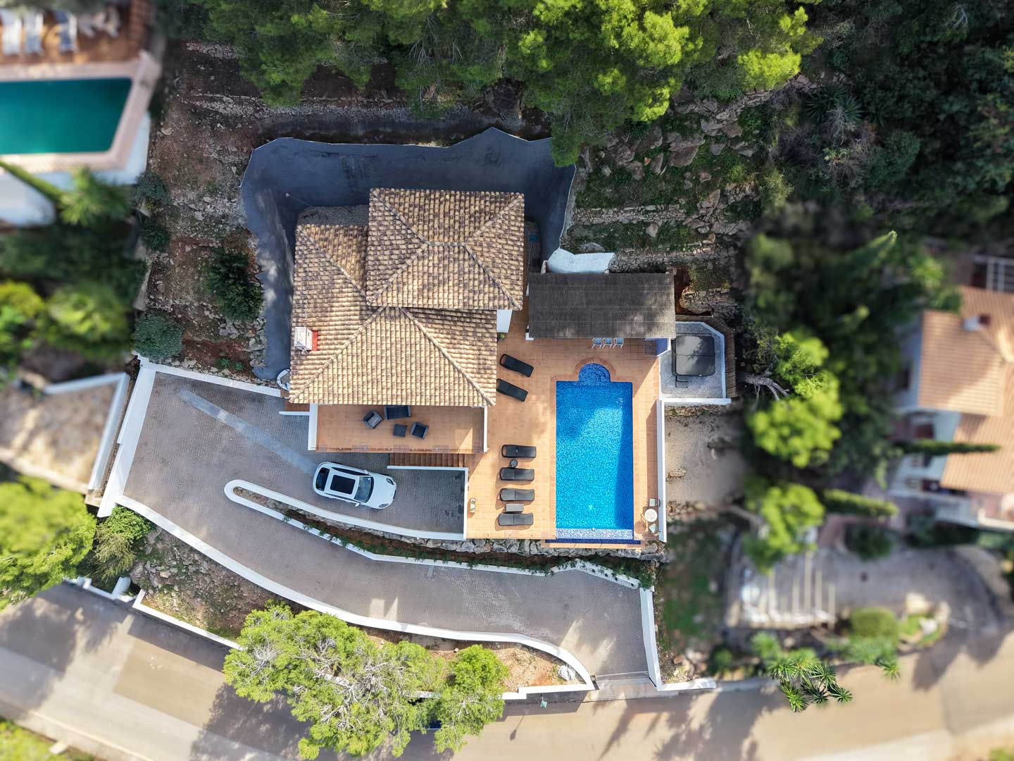 Luftaufnahme der Villa mit mediterranem Ziegeldach, rechteckigem Pool, Sonnenterrasse mit Liegen, Außen-Whirlpool und privater Einfahrt inmitten von Pinien.