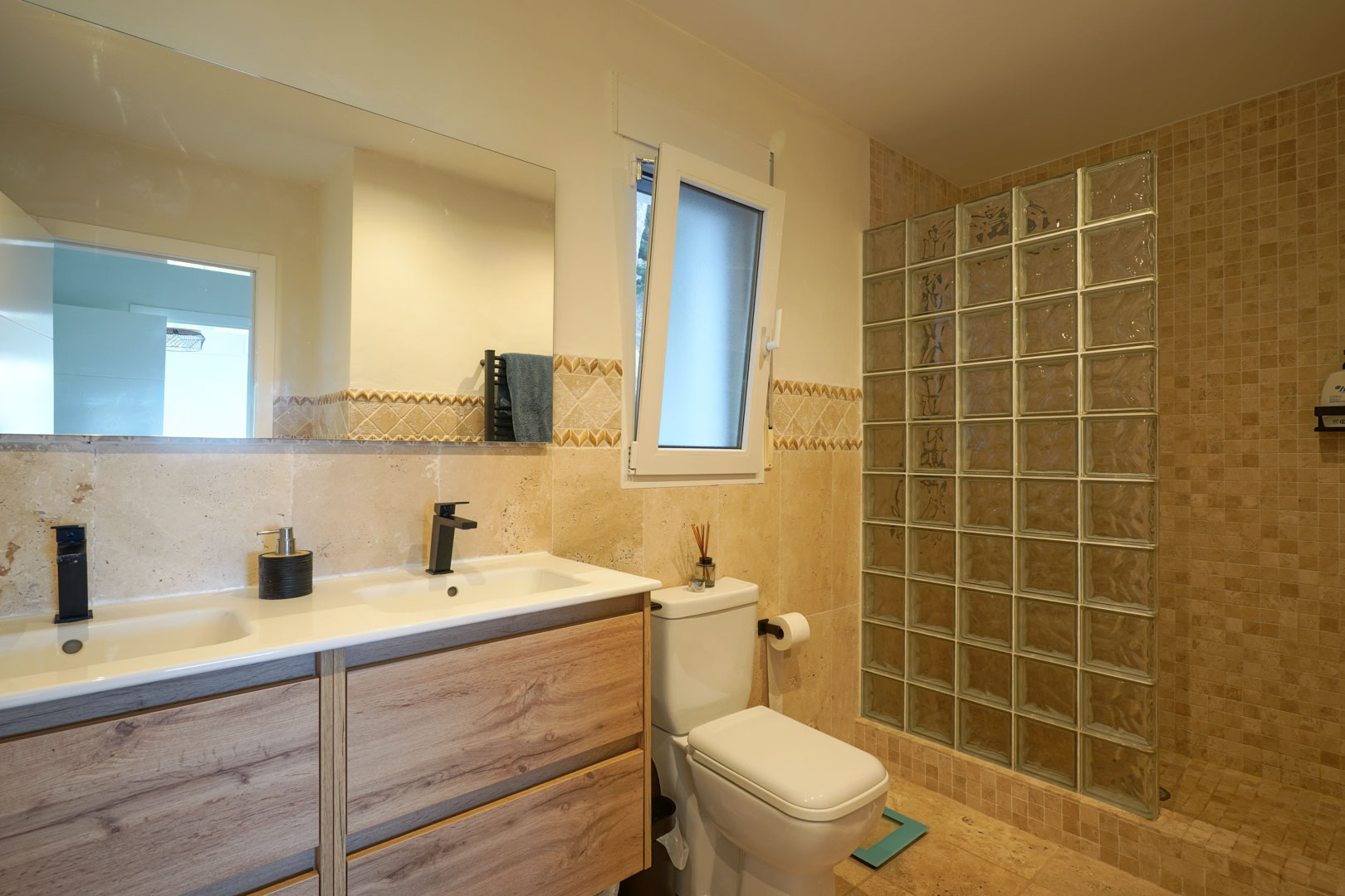 Modernes Badezimmer mit Doppelwaschtisch in Holzoptik, schwarzen Armaturen und einer Dusche mit Glasbausteinwand.