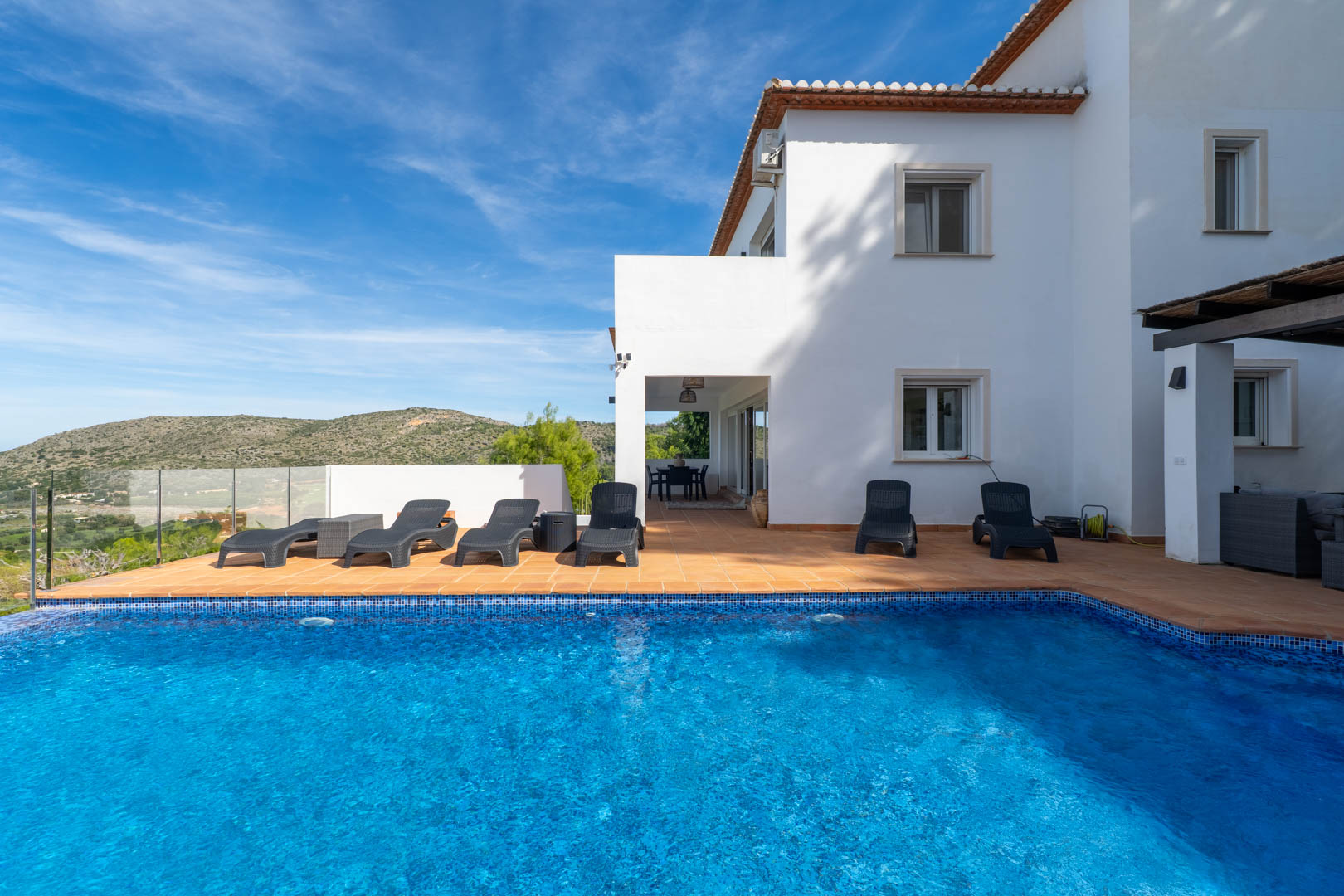 Privater Pool mit blauen Mosaikfliesen, umgeben von einer Terrakotta-Terrasse mit Sonnenliegen und weitem Blick auf die umliegende Berglandschaft.