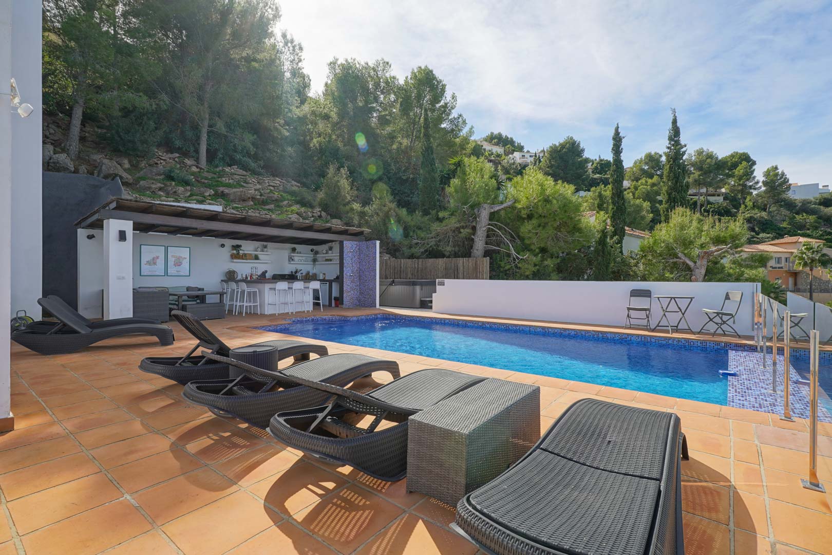 Privater Poolbereich mit Terrakotta-Fliesen, Rattan-Sonnenliegen und einer Außenbar unter einer Holzpergola, umgeben von einer natürlichen Waldlandschaft.