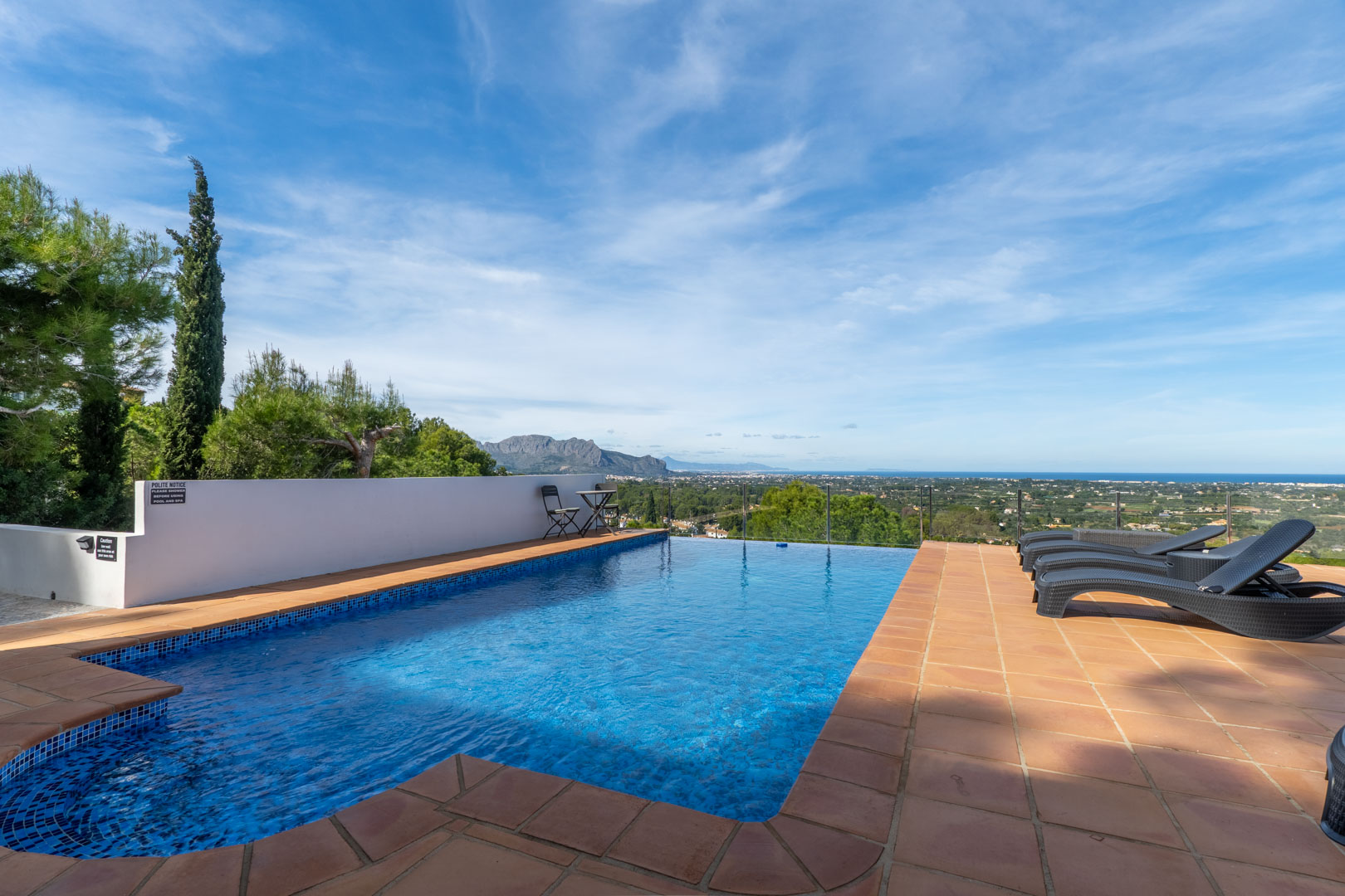 Schwimmbad mit blauen Mosaikfliesen und Terrakotta-Terrasse, mit Panoramablick auf das Mittelmeer und das Montgó-Massiv.