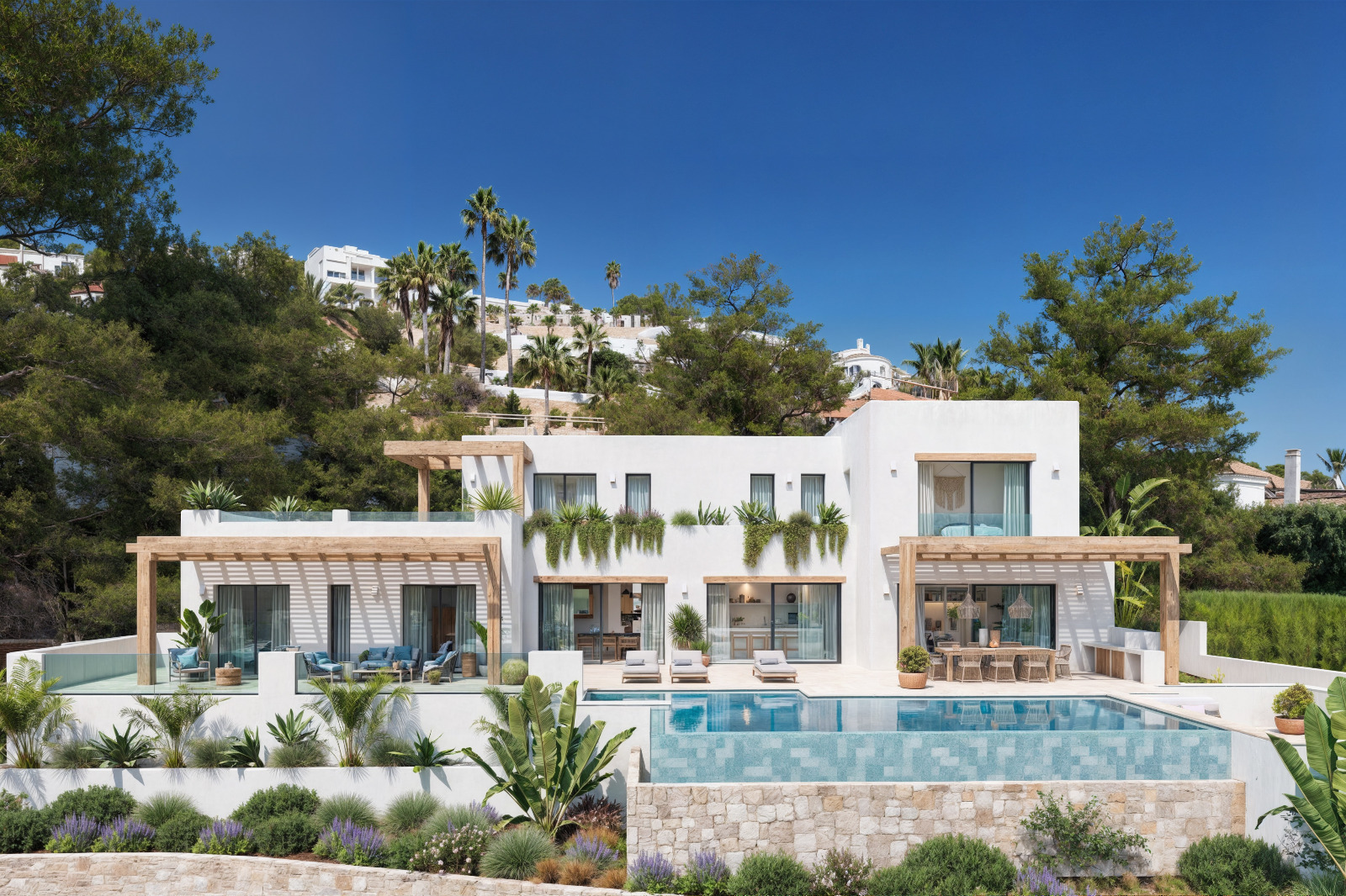 Außenansicht der Villa mit weißen Fassaden, Holzpergolen, einem Infinity-Pool und einem mediterranen Garten mit Natursteinmauern.