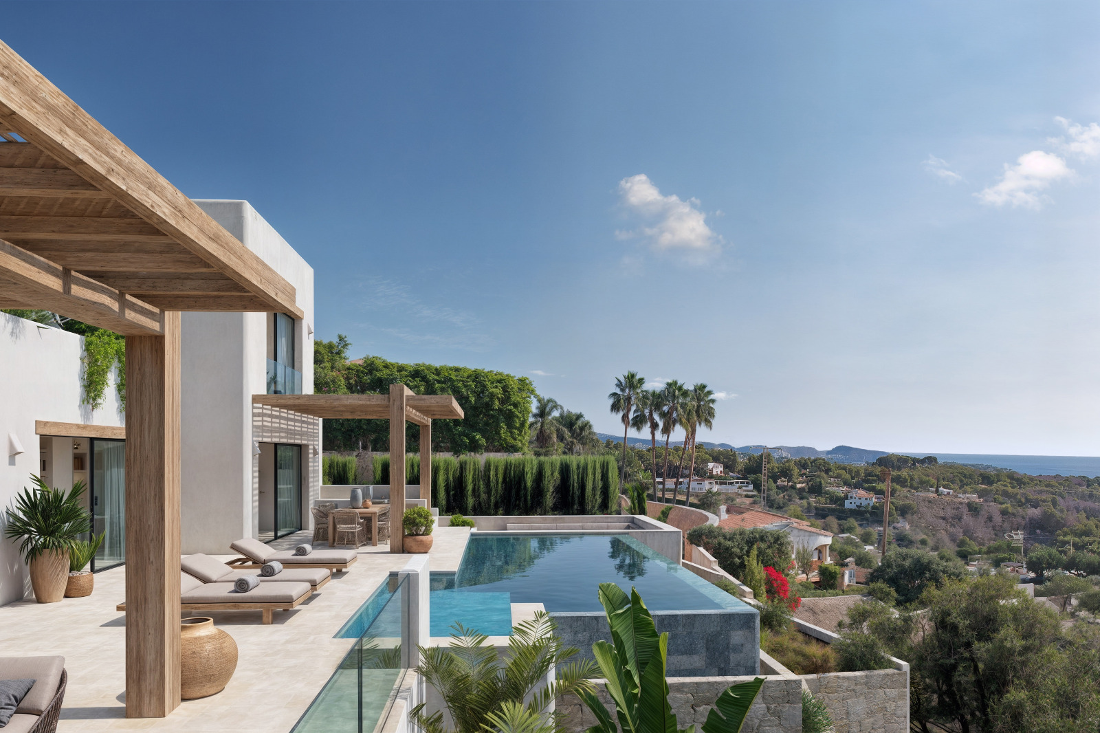 Außenbereich mit Infinity-Pool, Holzpergolen und Panoramablick auf das Meer. Die weiße Fassade im Ibiza-Stil fügt sich in die mediterrane Vegetation ein.