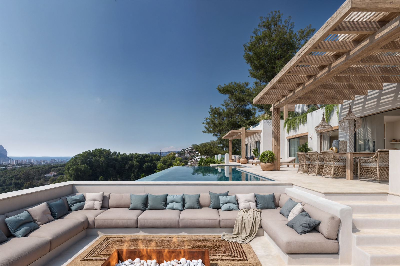 Versunkener Loungebereich mit Feuerstelle, Holzpergola über dem Essplatz und Infinity-Pool mit weitem Blick auf das Mittelmeer und den markanten Peñón de Ifach.