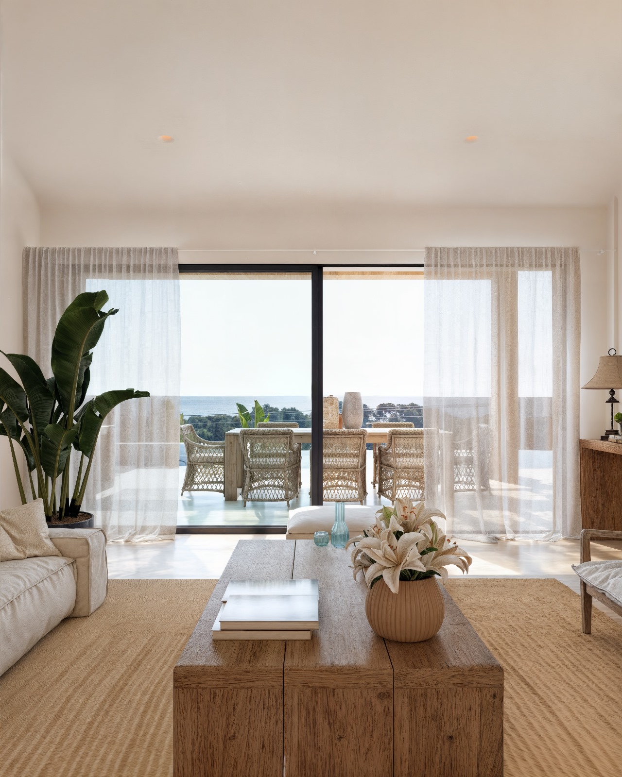 Wohnbereich im Ibiza-Stil mit Naturholztisch und großen Schiebetüren, die auf eine Terrasse mit Essbereich und Meerblick führen.