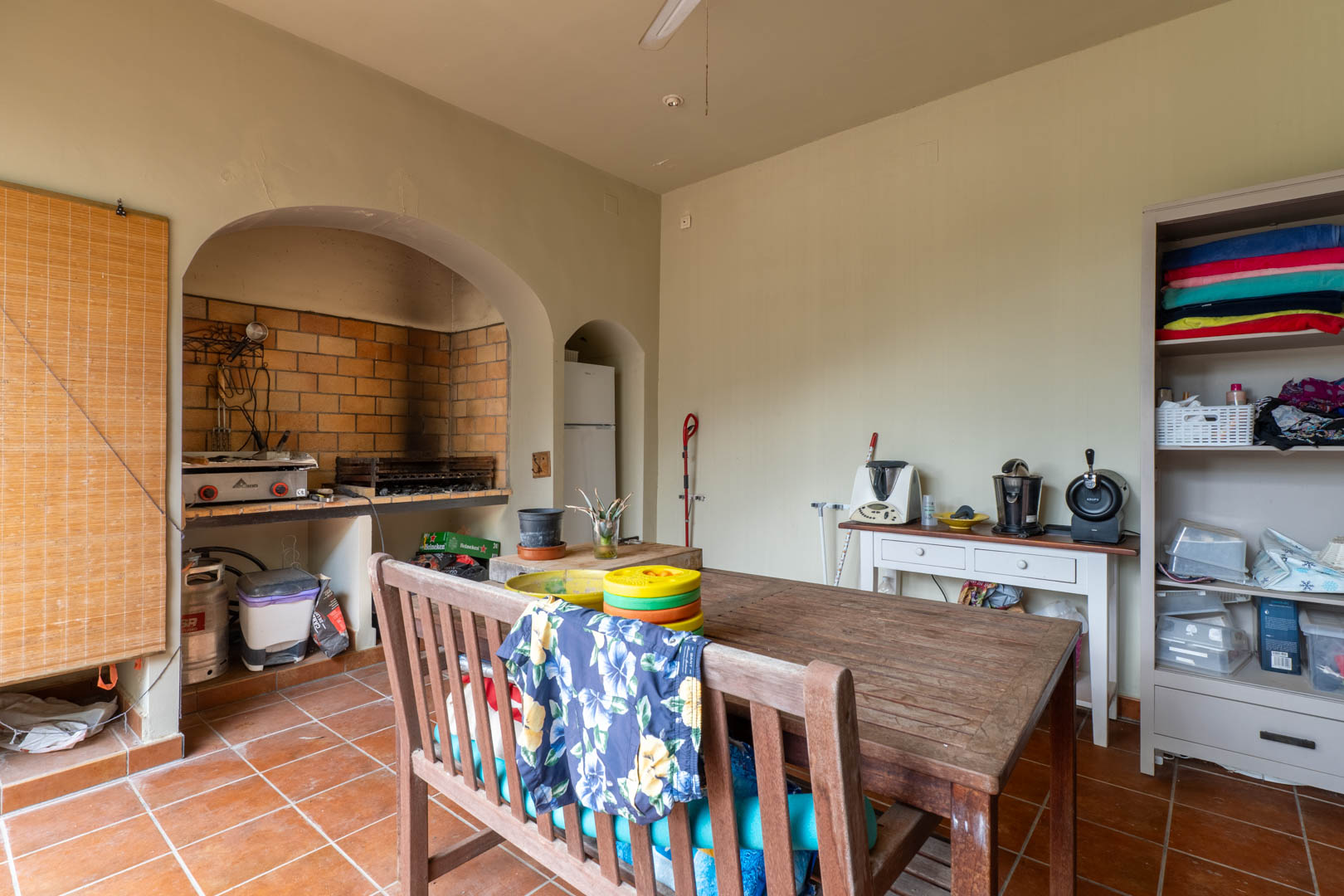 Außenküche mit gemauertem Grillkamin, rustikalem Holztisch und traditionellen Terrakottafliesen für Mahlzeiten im Freien.
