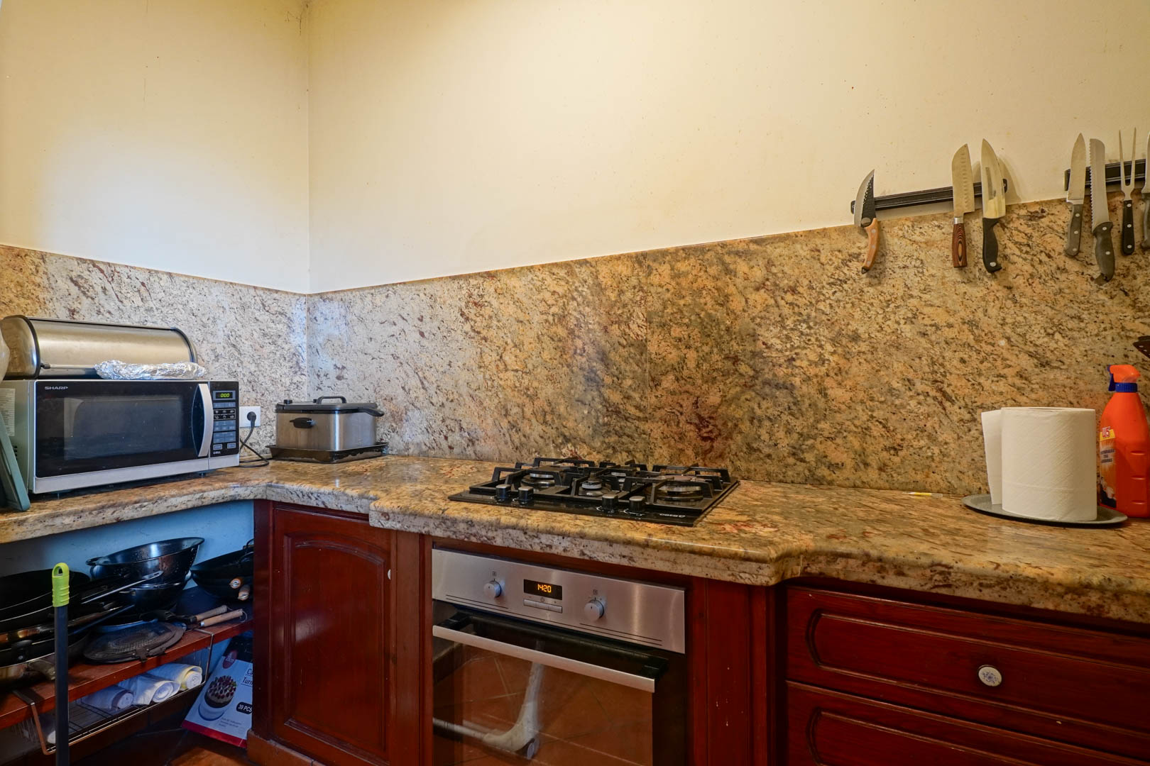 Küche mit Arbeitsplatte und Rückwand aus gemustertem Granit, ausgestattet mit Gaskochfeld, Edelstahlofen und Schränken aus dunklem Massivholz.