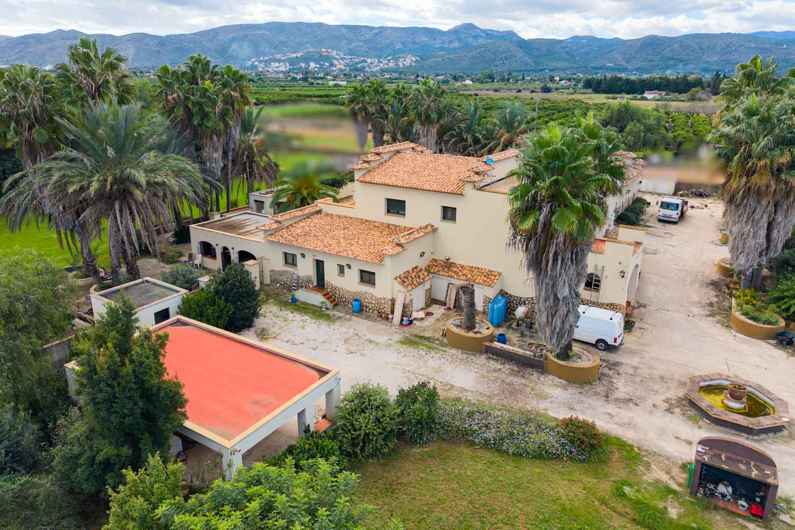 Luftaufnahme der mediterranen Villa mit Terrakottadächern, umgeben von Palmen und Gärten, mit weitem Blick auf das Tal und die Berge von Ondara.