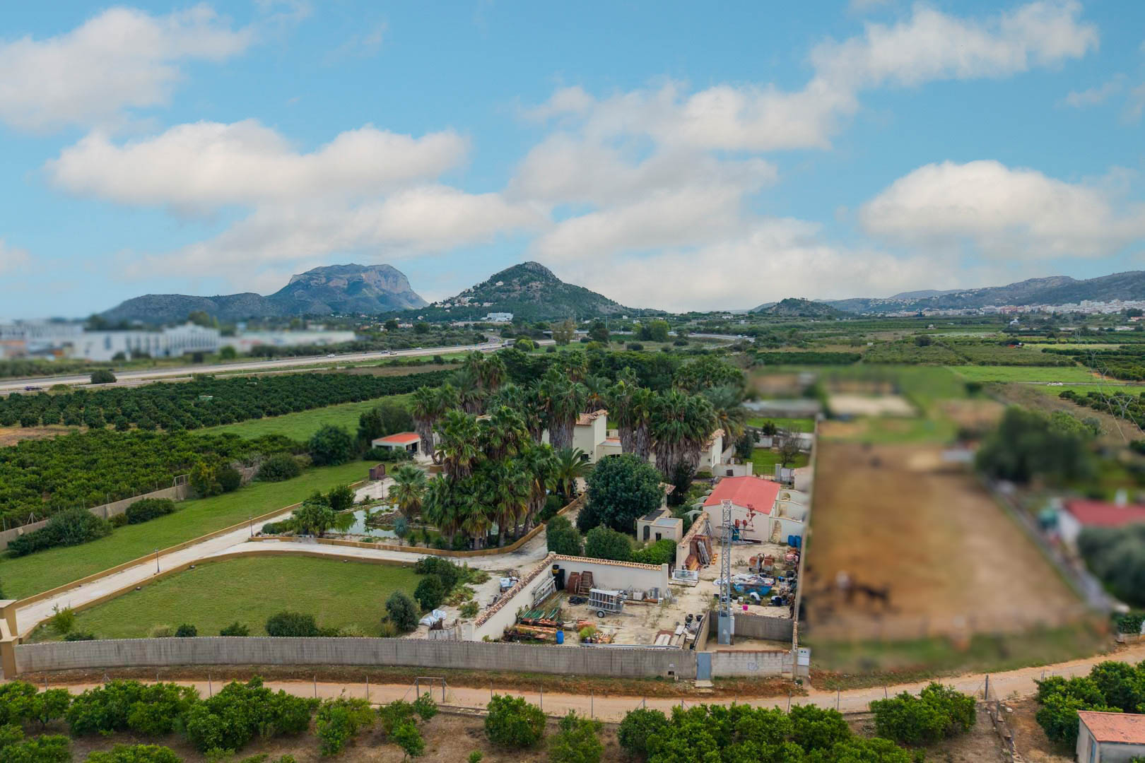 Luftaufnahme des 10.000 m2 großen Anwesens in Ondara mit weitläufigen Palmengärten, einem zentralen Teich und Panoramablick auf die umliegenden Berge.