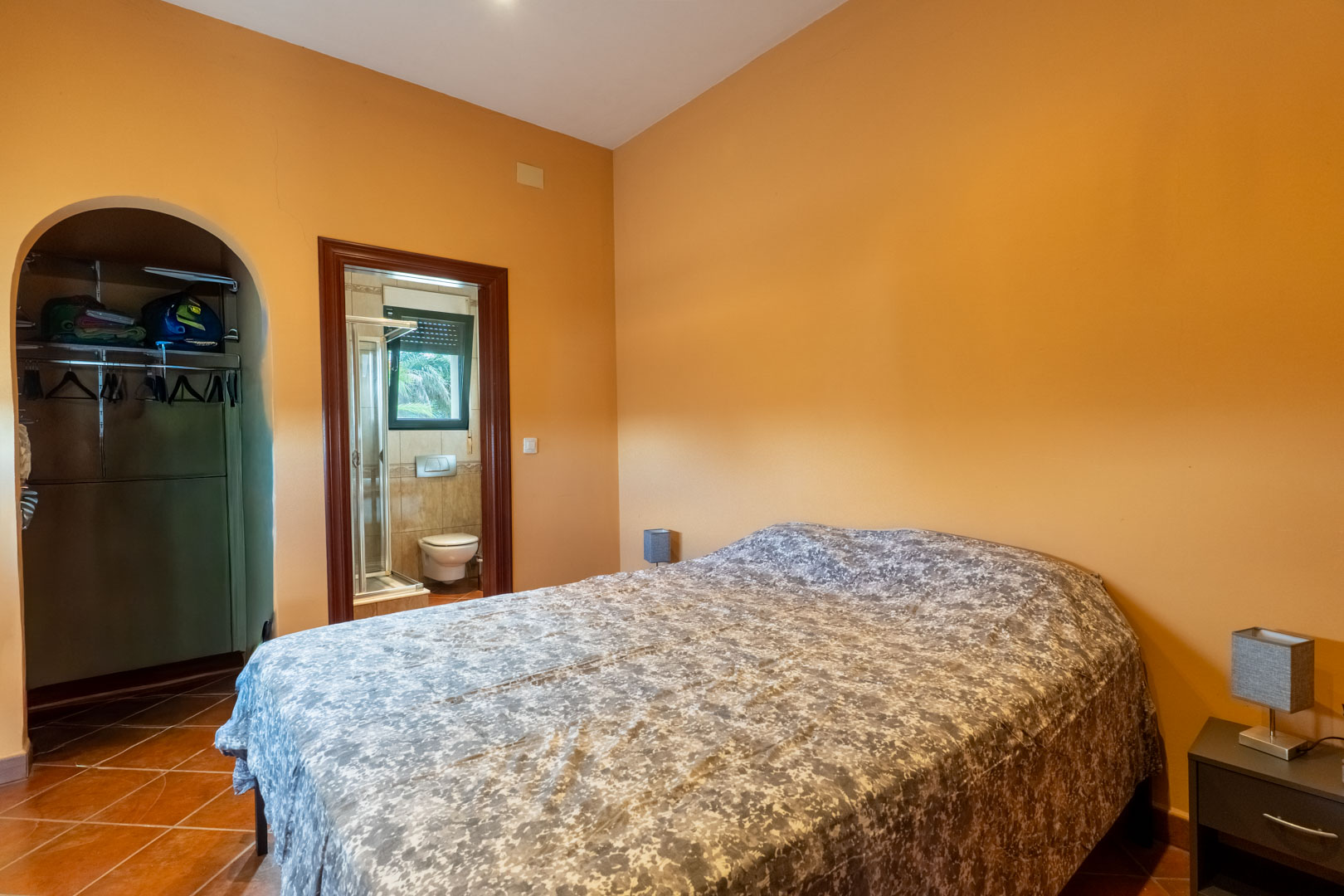 Schlafzimmer mit Terrakottaboden und ockerfarbenen Wänden, ausgestattet mit einem begehbaren Kleiderschrank und En-Suite-Badezimmer.