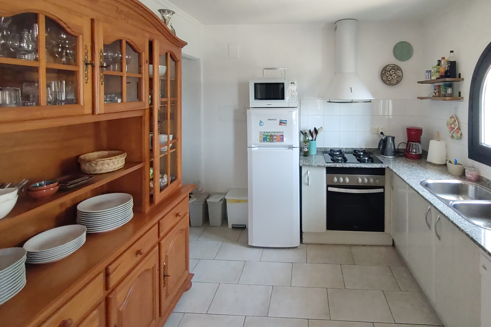 Funktionale Küche mit Granitarbeitsplatte, Gaskochfeld und einem großen Massivholz-Buffetschrank, ergänzt durch helle Fliesenböden.