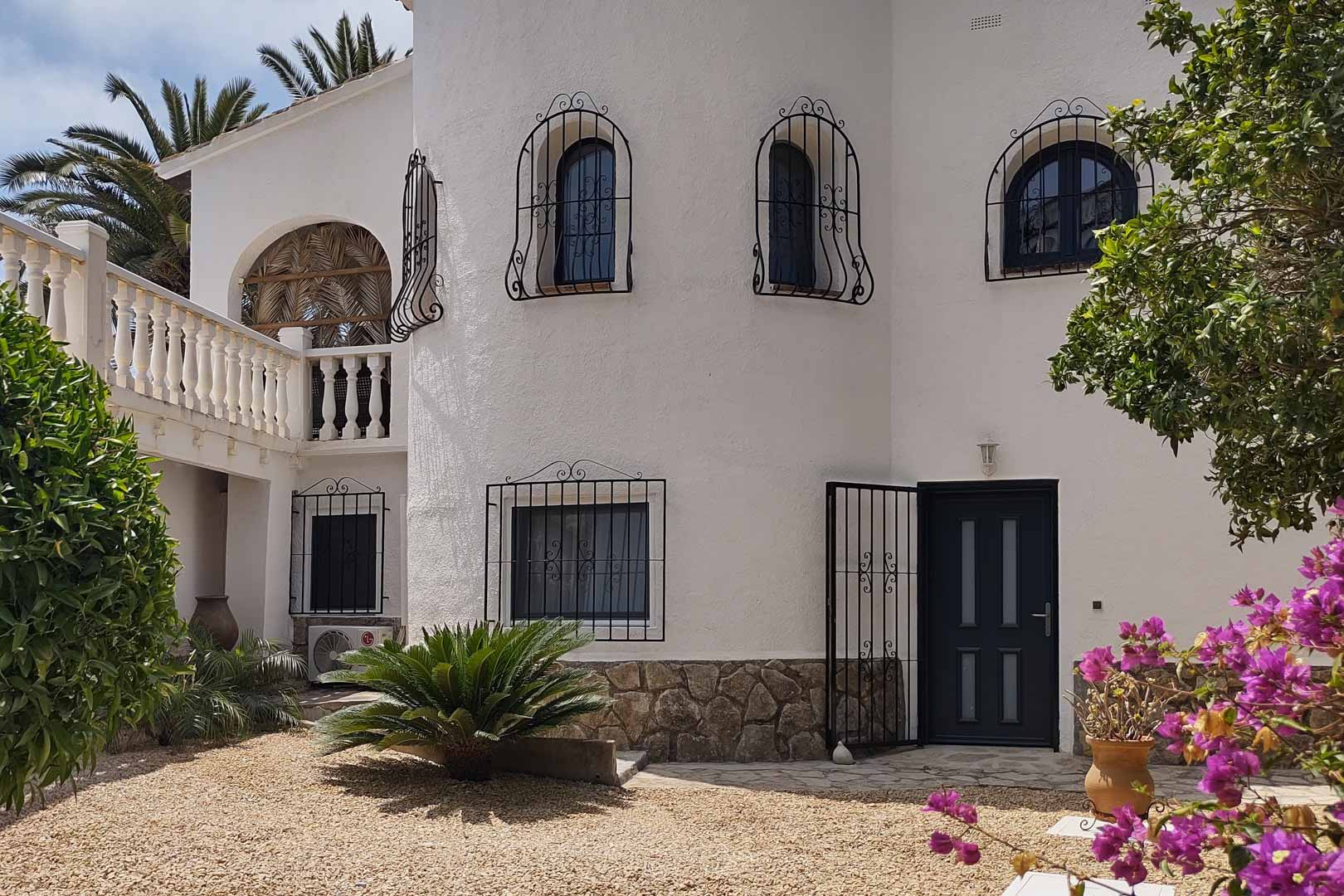 Mediterrane Außenfassade mit weißem Putz, Steinsockel, dekorativen schmiedeeisernen Fenstergittern und einem Kiesgarten-Eingangsbereich mit blühenden Bougainvilleen.