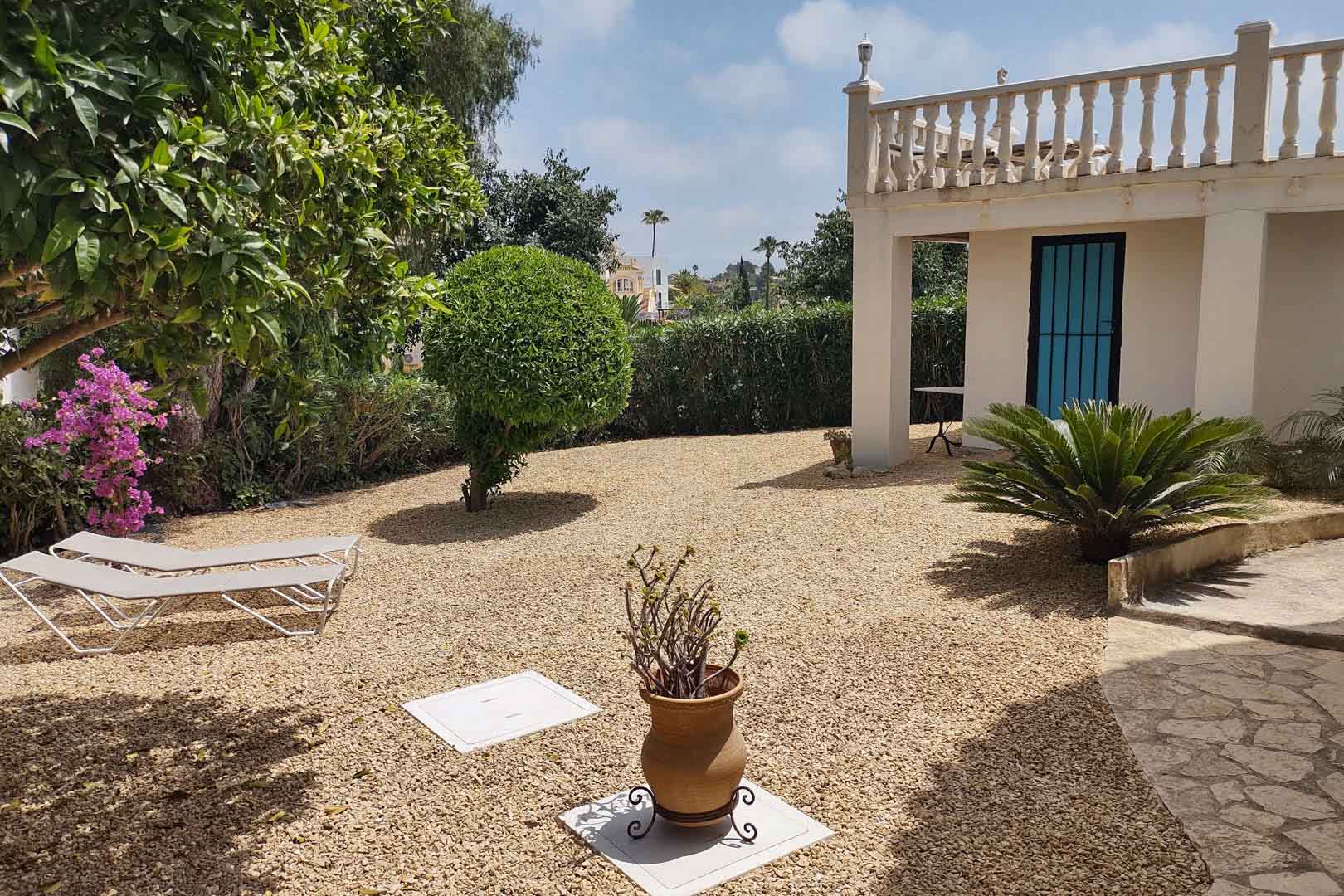 Pflegeleichter mediterraner Garten mit Kiesfläche, Sonnenliegen, einheimischen Pflanzen und weißer Fassade mit klassischer Steinbalustrade.