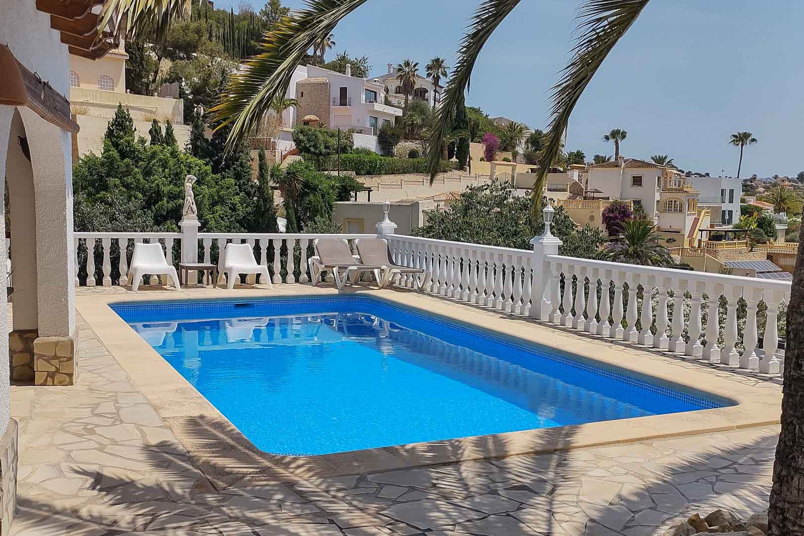 Rechteckiger Pool mit blauen Mosaikfliesen, eingefasst von einer Natursteinterrasse und weißer Balustrade mit weitem Blick über die mediterrane Landschaft.